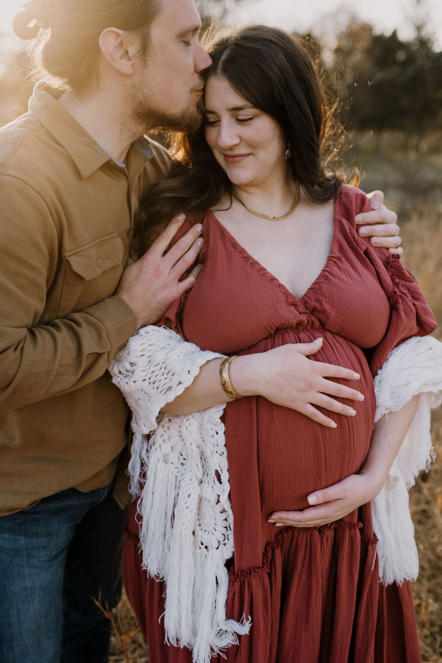 Man embraces and kisses pregnant woman at golden hour