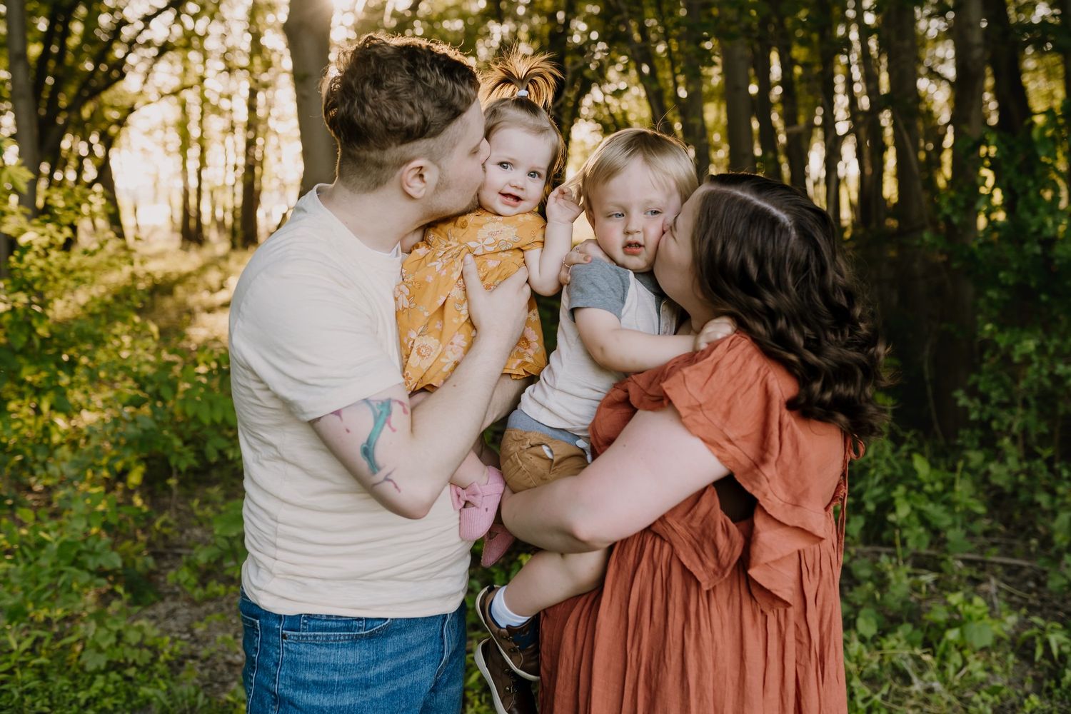 Family of four poses while parents kiss their toddlers