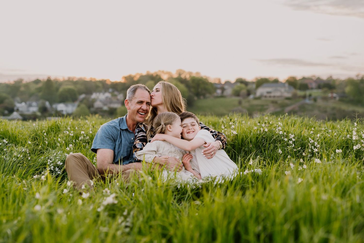 Family sits in a flower field for family photos while kids snuggle and mom kisses dad's head