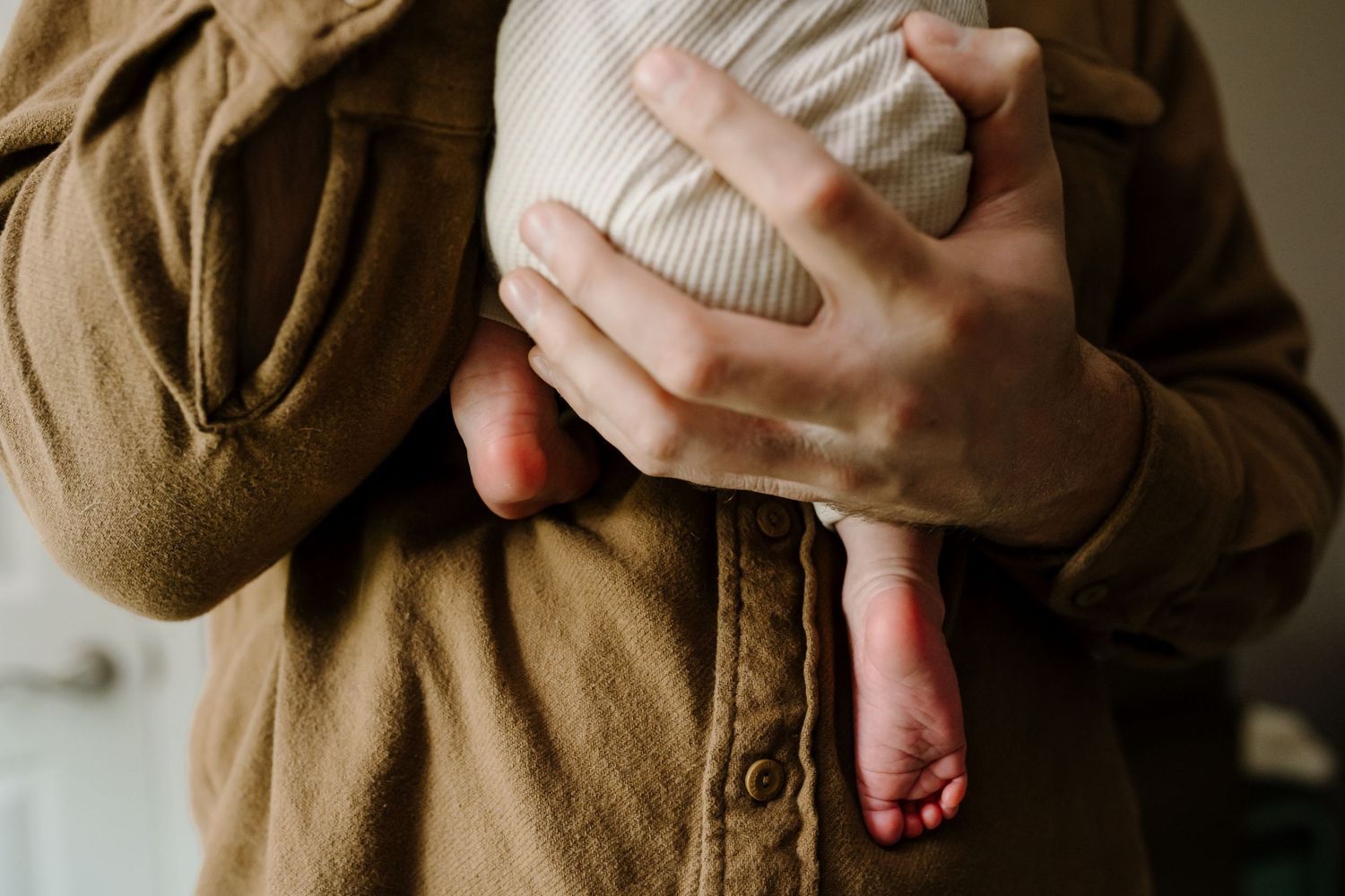 Dad's hands holding newborn with little feet dangling