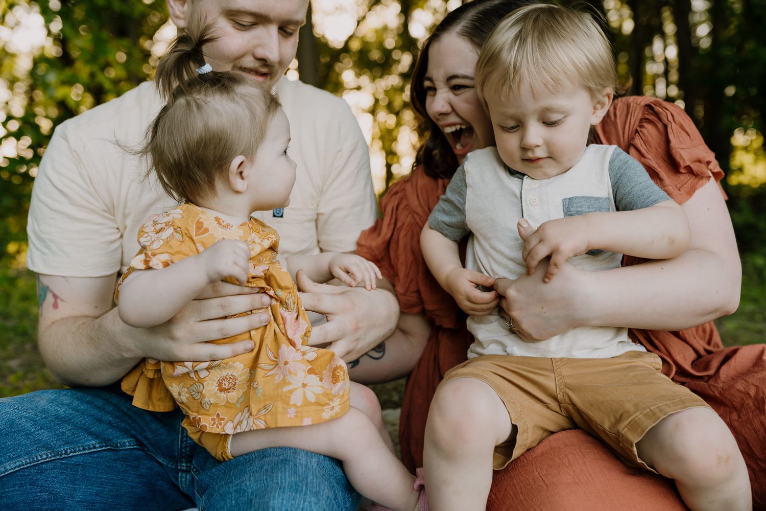 Parents sit on blanket and hold their two small children and play with them