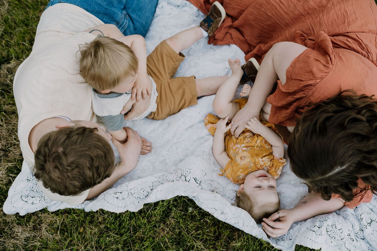 Parents lay on blanket and tickle their toddlers during outdoor family pictures