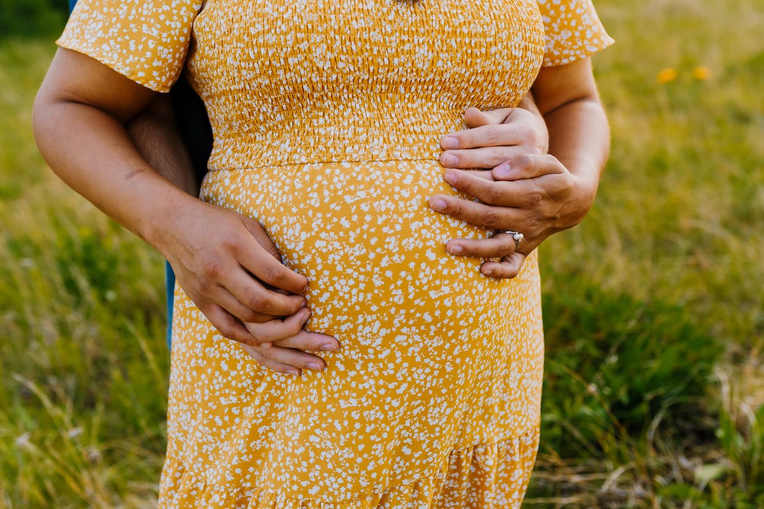 Husband embraces pregnant wife from behind, photo of their hands on her belly