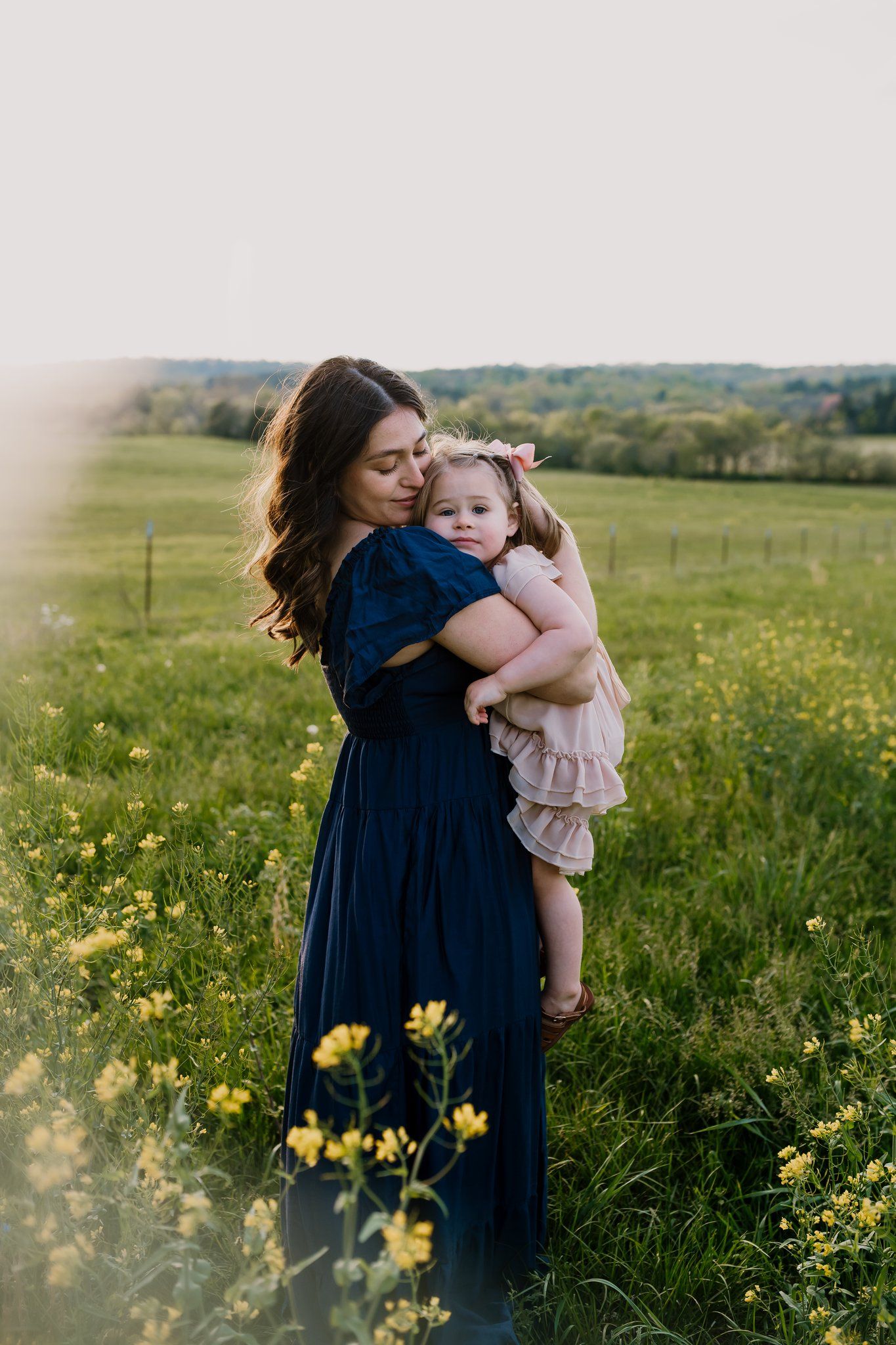 Pregnant mom snuggles her toddler in a field of yellow flowers