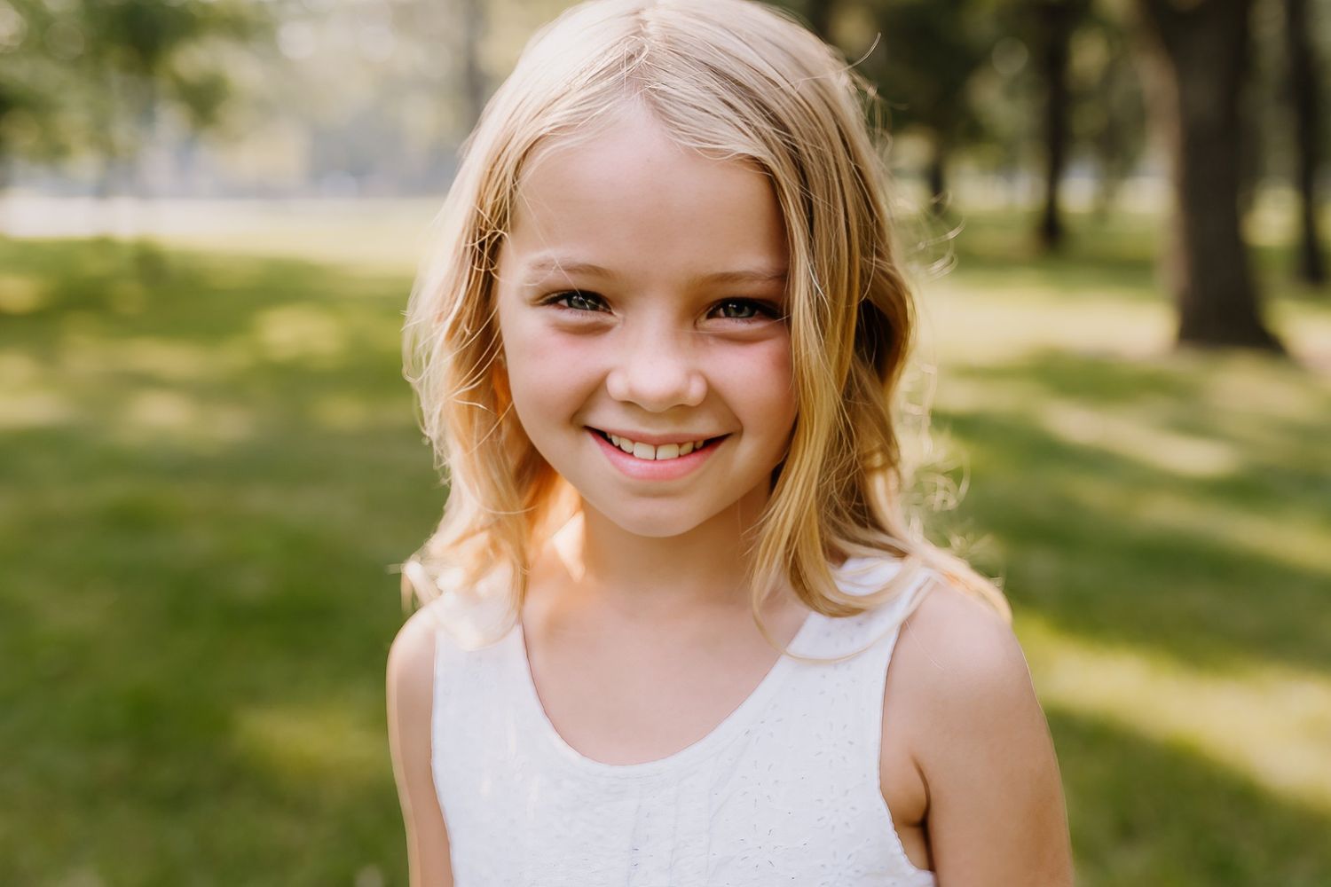 Little girl with blonde hair and white dress smiles at the camera