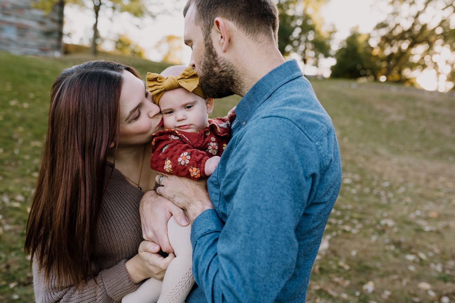 Mom and dad kiss baby girl at sunset family photoshoot