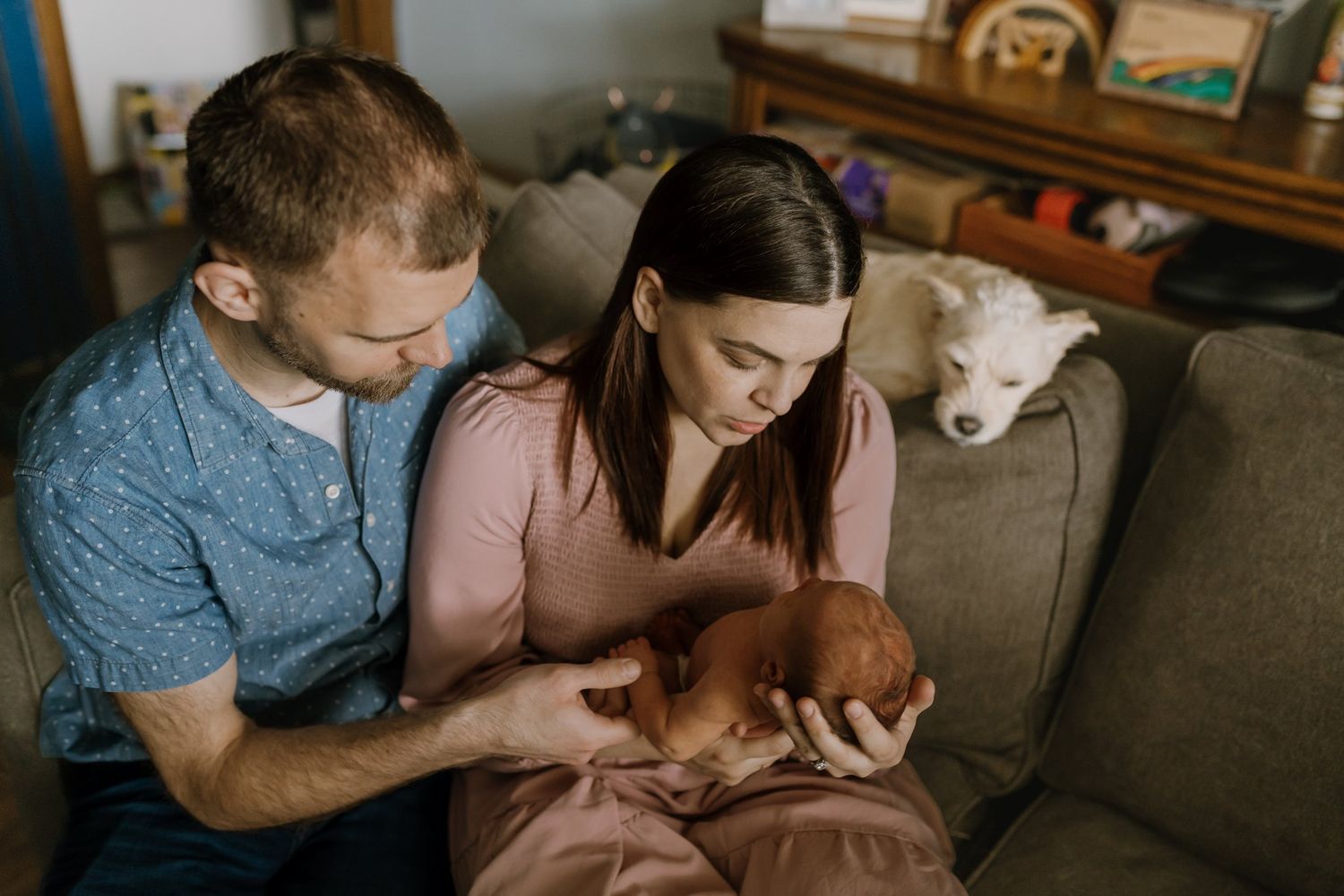 Mom and dad sit on couch and hold their newborn daughter