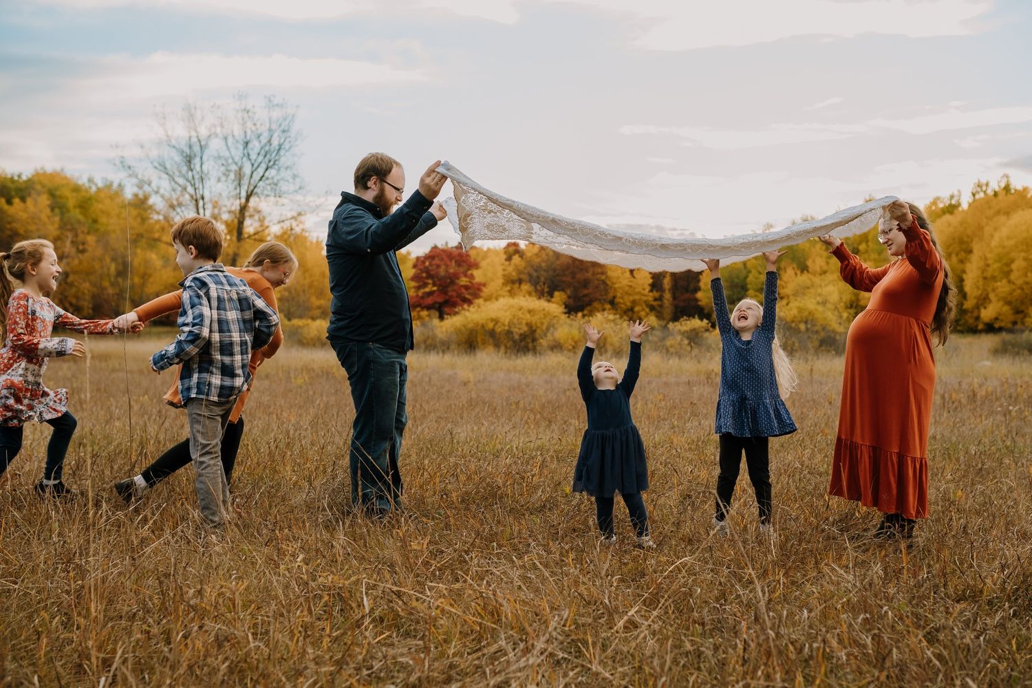 Large family playing with a blanket in an autumn field with colorful fall foliage.