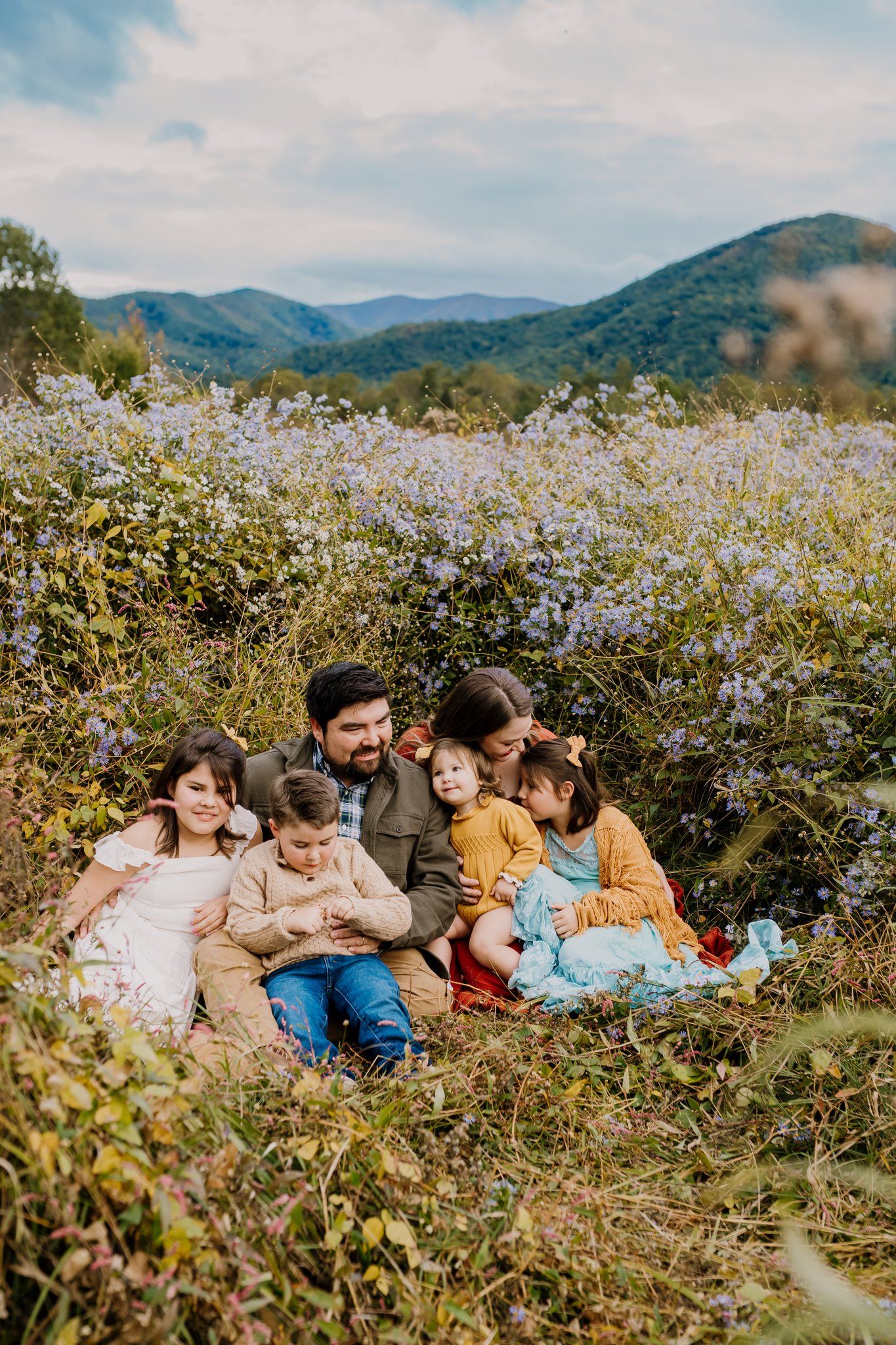 Family of six sits in a grassy field of flowers in Cades Cove and snuggles together happily