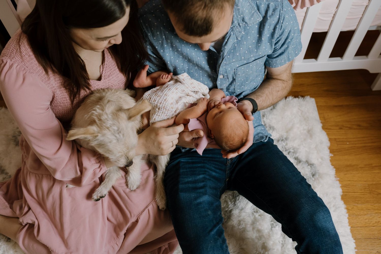 Parents sit on nursery floor holding newborn and dog