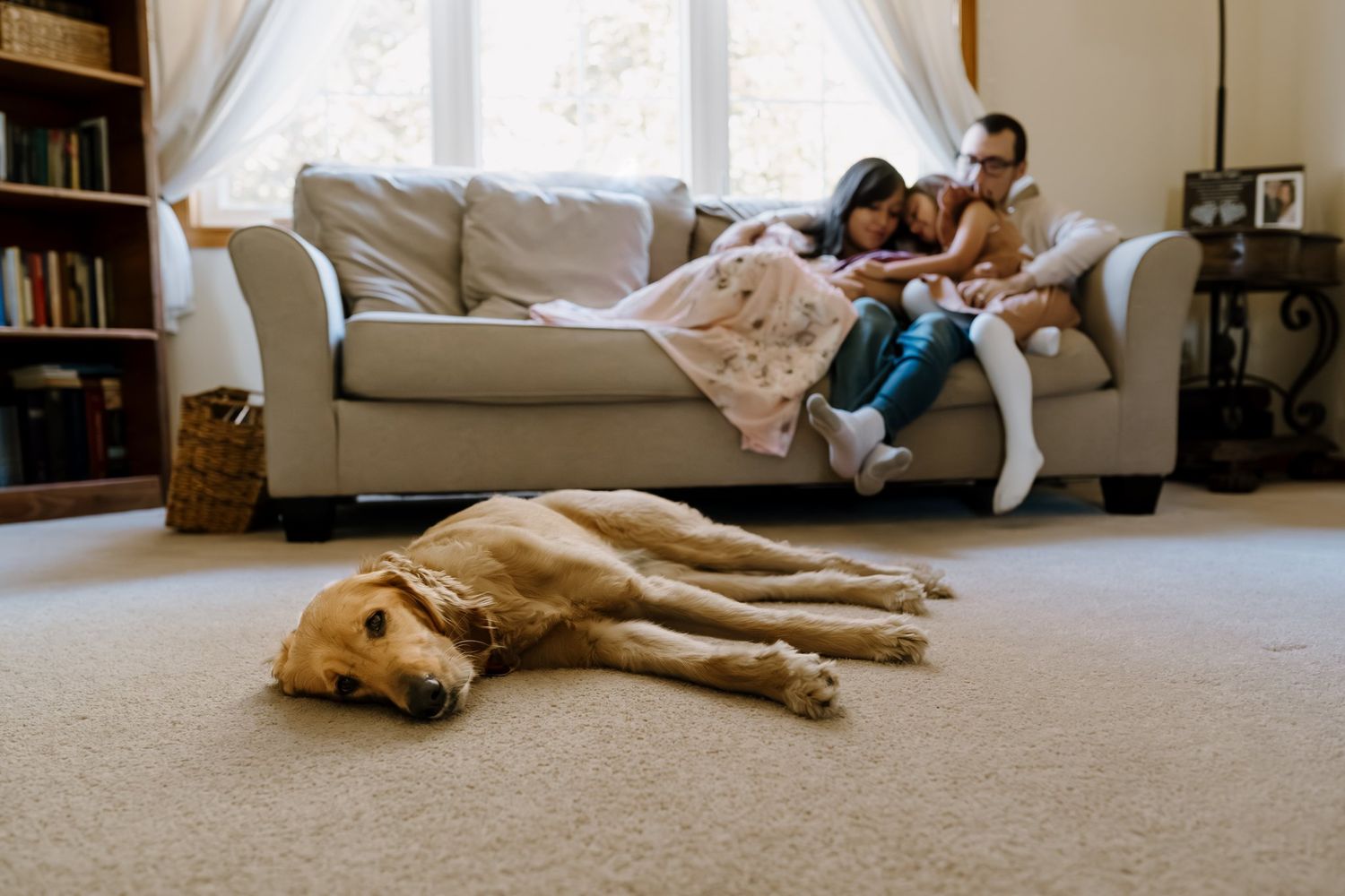 Family sits on couch with newborn while dog sleeps in front of them