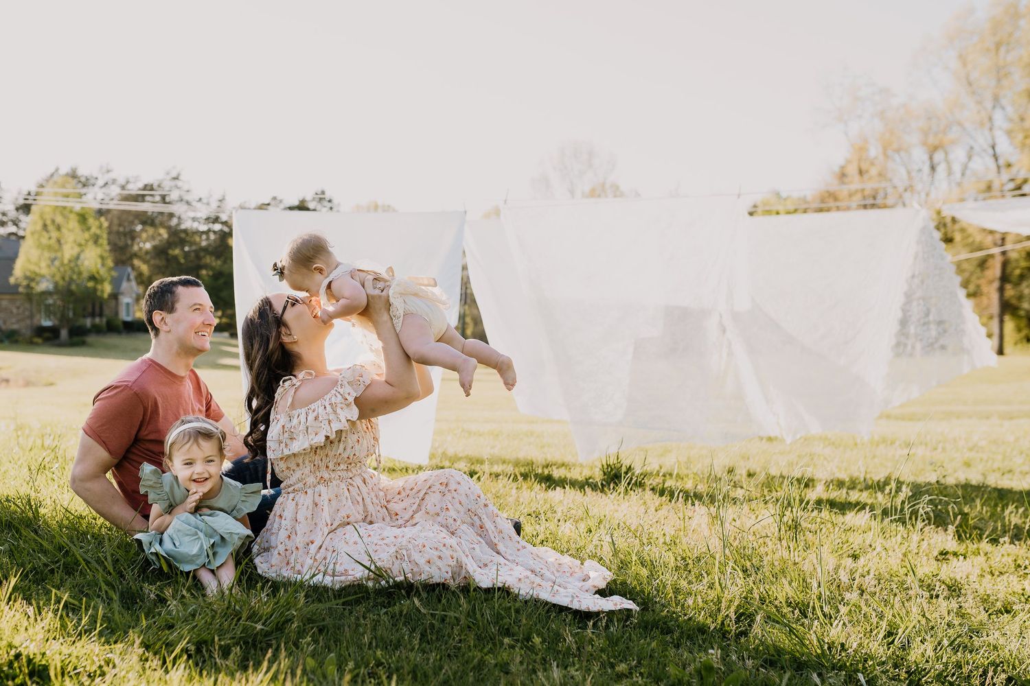 Mom sits in the grass with her family in front of clothesline setup