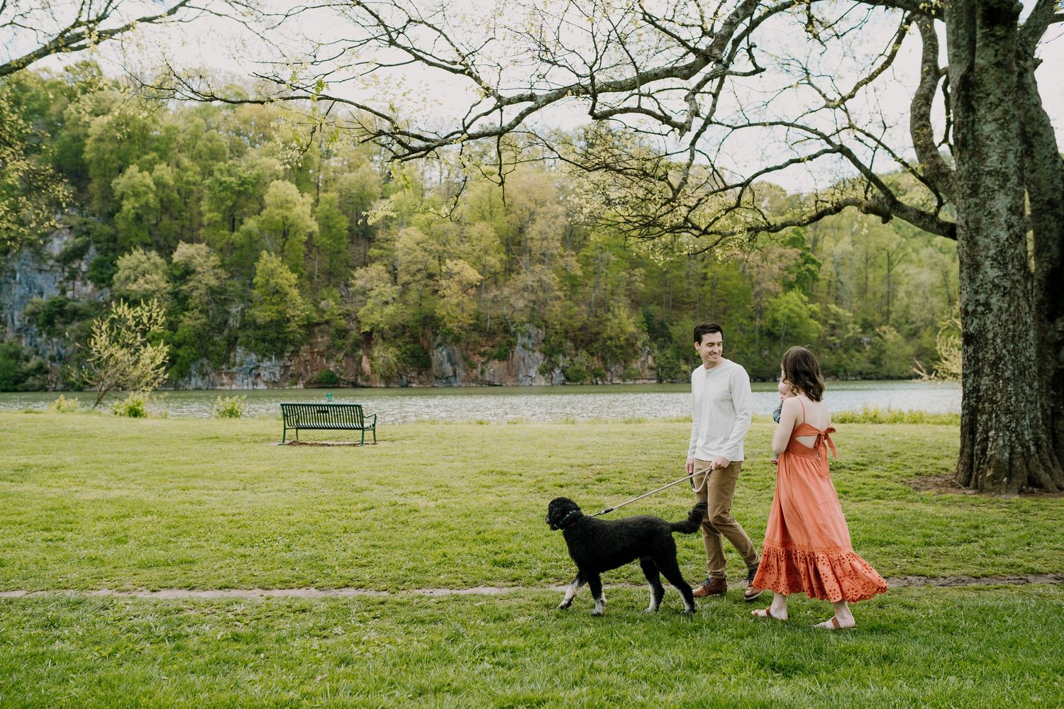 Man and woman walk through a park with their dog and baby