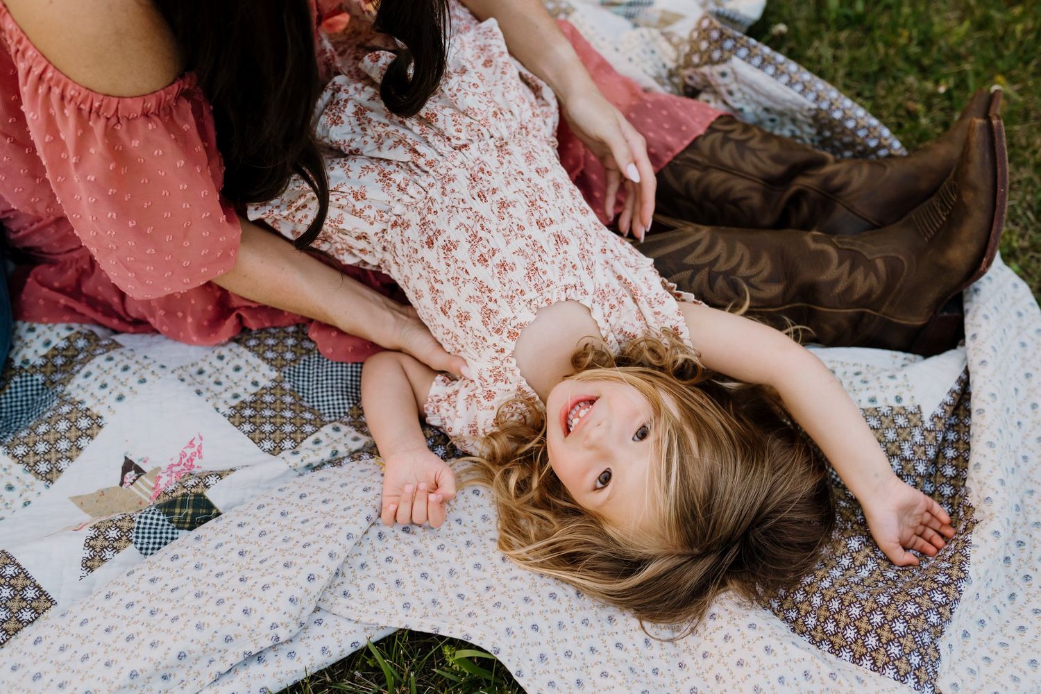 Toddler girl lying on a quilt blanket outdoors looking up and smiling.