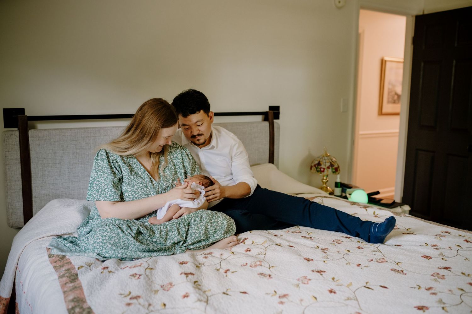 Man and woman sit on their bed and look at their newborn