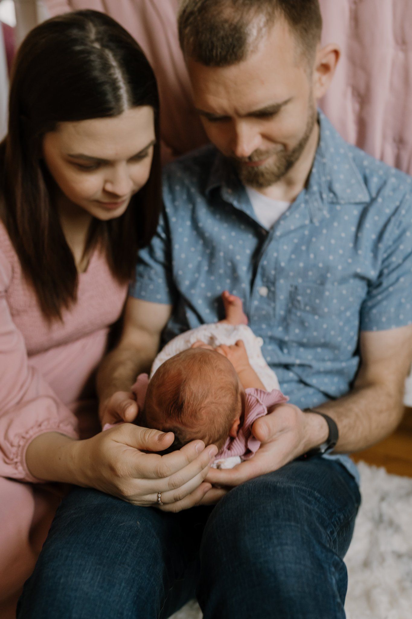 Mom and dad gaze lovingly at their newborn as they sit in her nursery