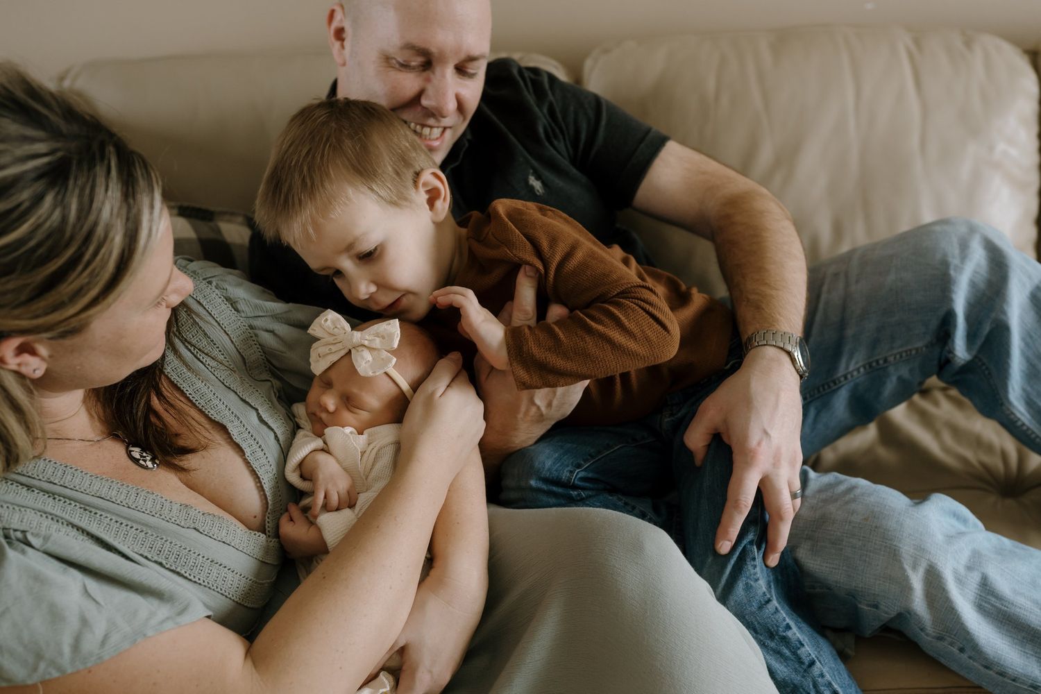 family sits on couch and dotes on newborn baby girl during in home newborn pictures in saint cloud minnesota
