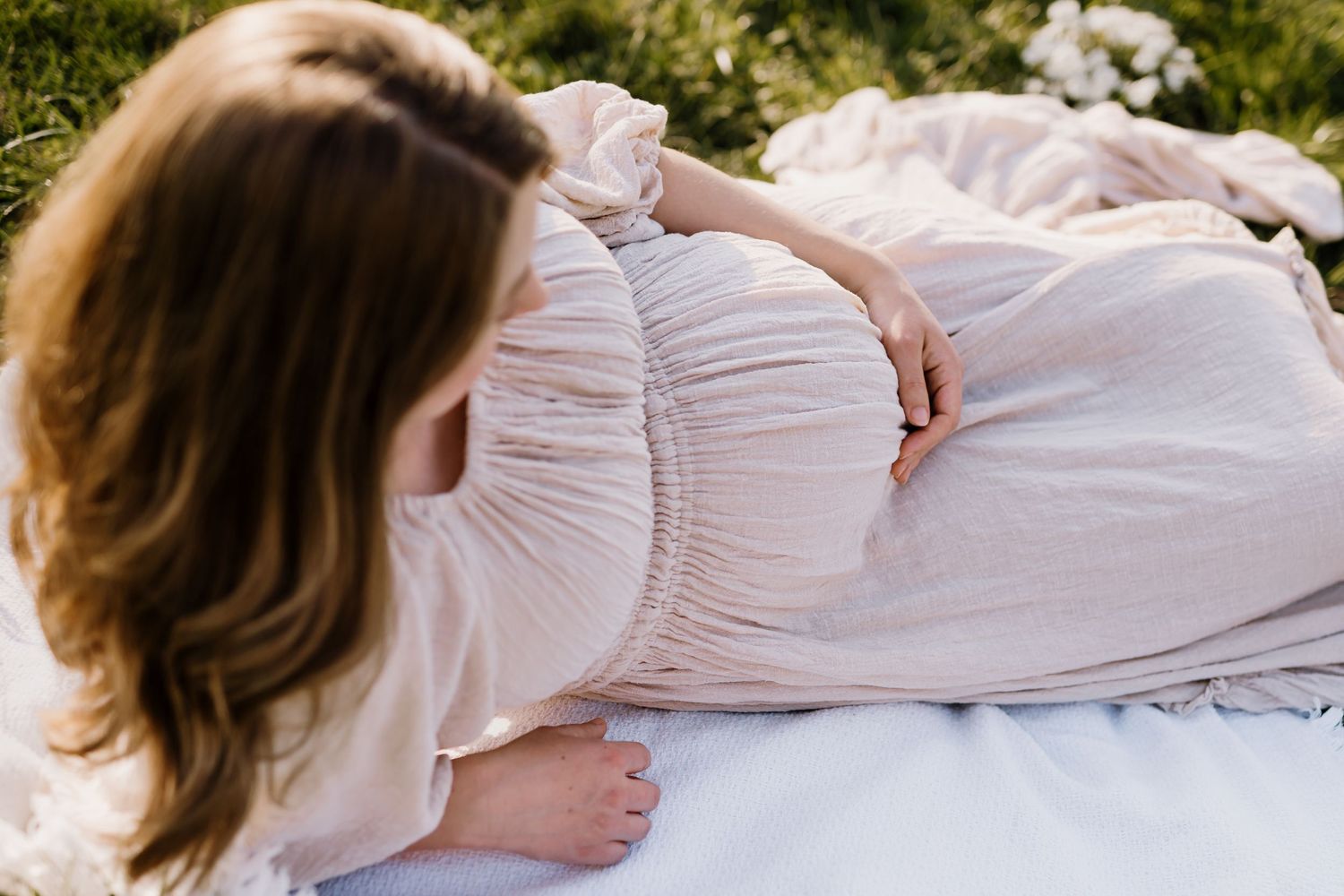 Pregnant woman lays on the ground and looks down at her belly