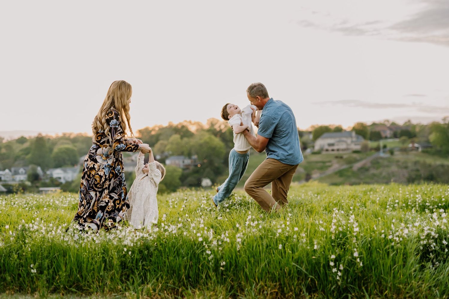 Family of four plays happily together in a flower field for fun family photos