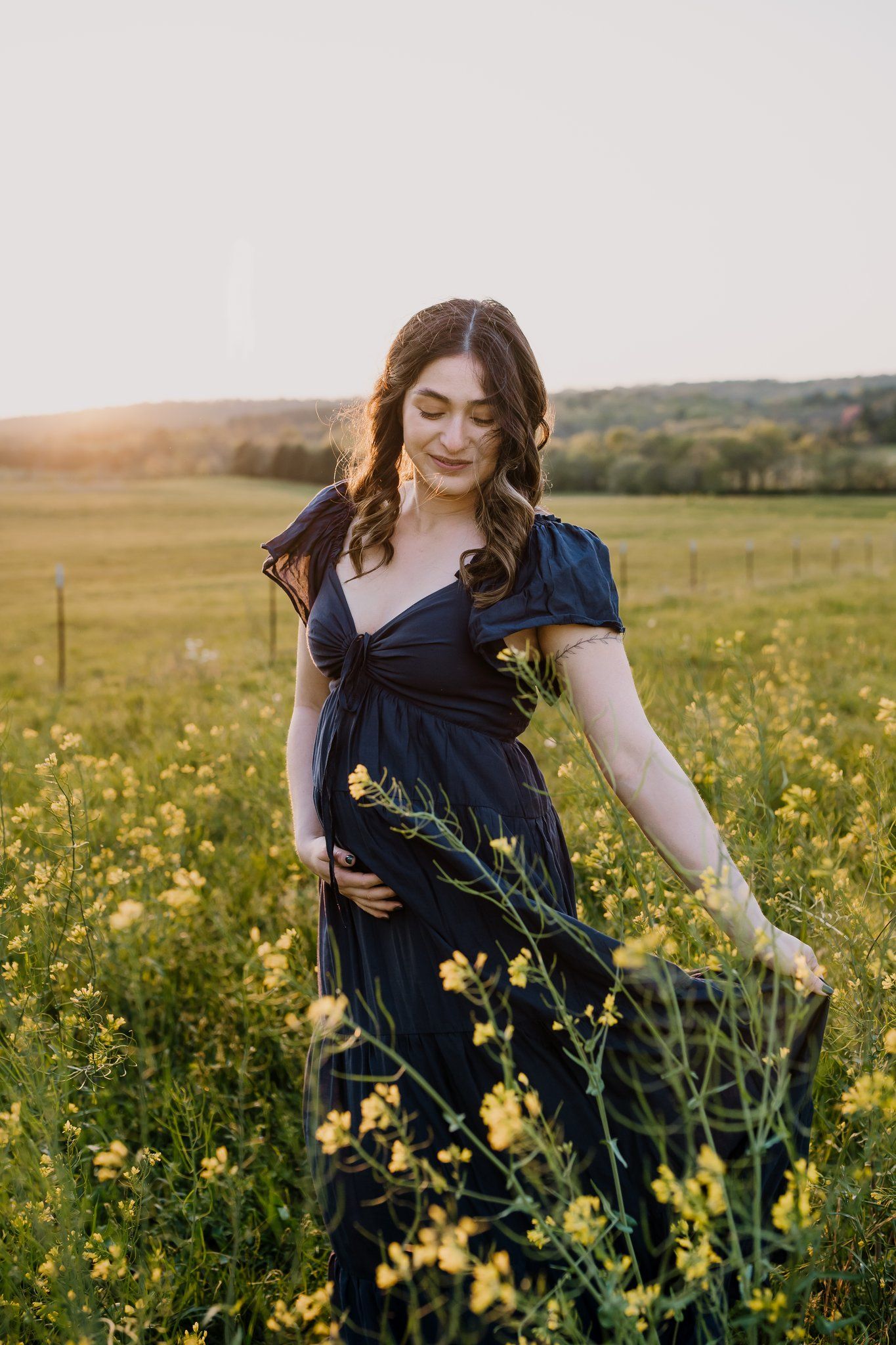 Pregnant mom cradles her belly while swishing her skirt in a field of yellow flowers
