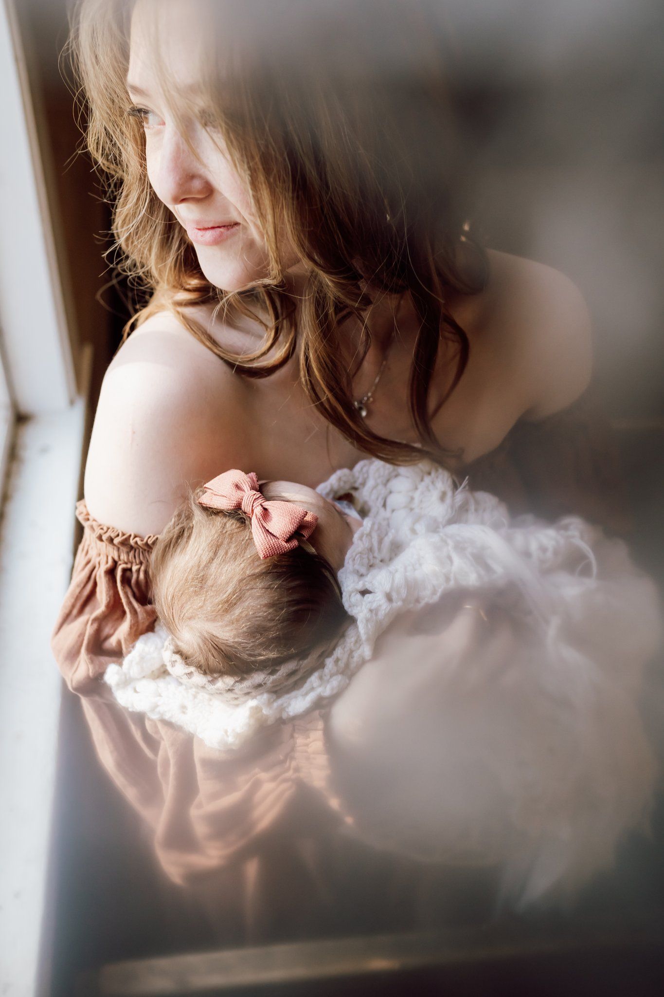 mom smiles and looks out window while holding daughter