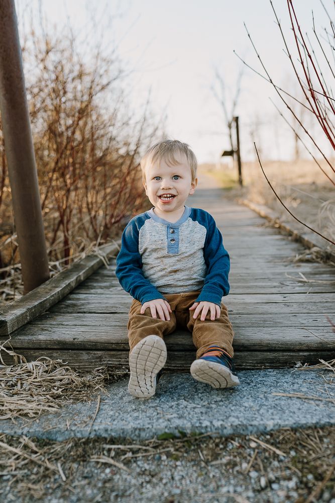 toddler sits on bridge and smiles at camera during minnesota lifestyle photo shoot