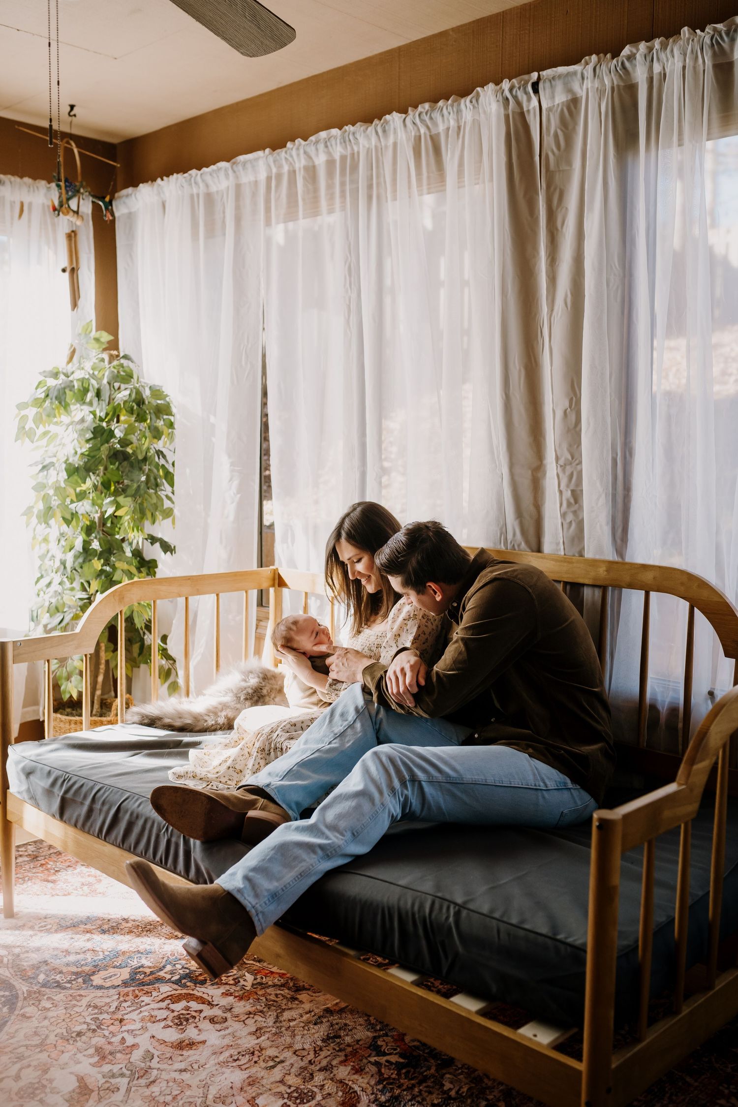 Man and woman sit on a daybed in their home and play with their newborn