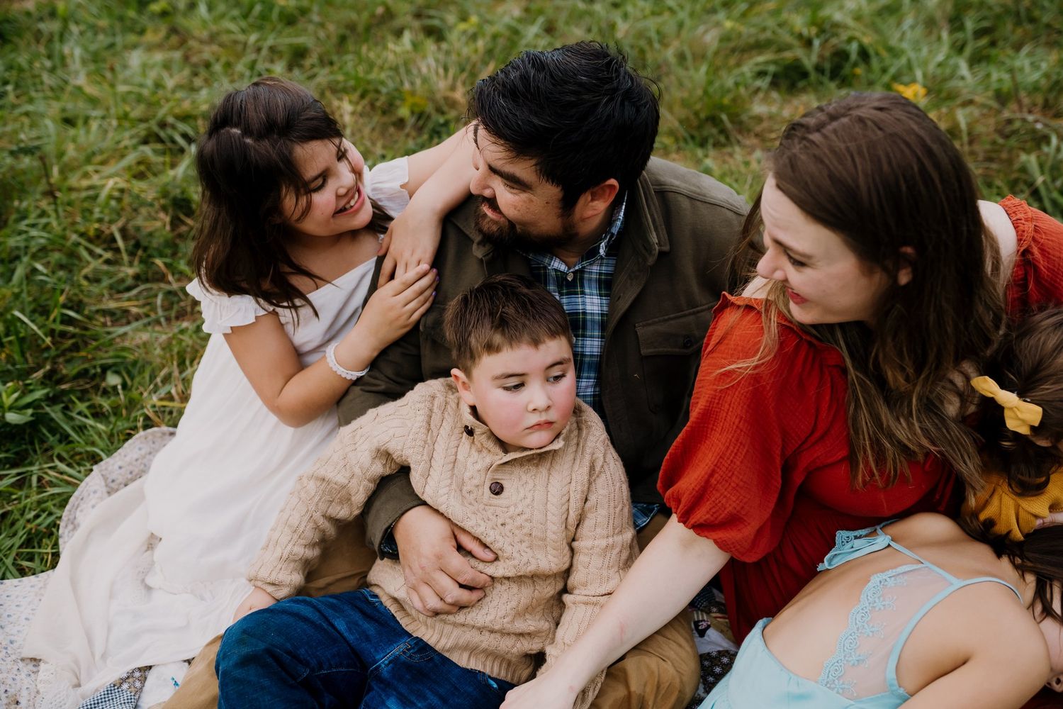 Family sits together on a blanket and parents look at the oldest daughter who is telling a story