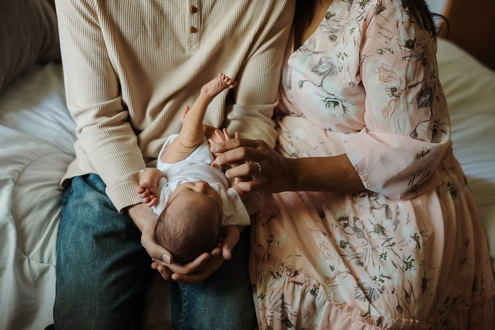 parents sit on bed and play with baby's hand