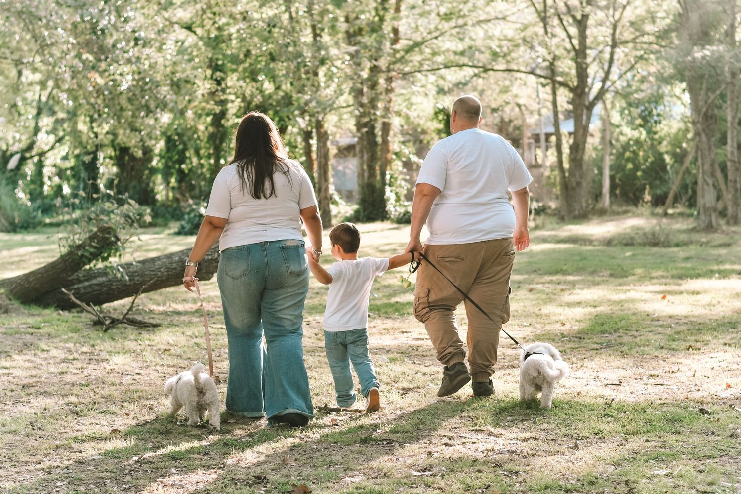 Family walking together on wooded path with their dog on sunny day.