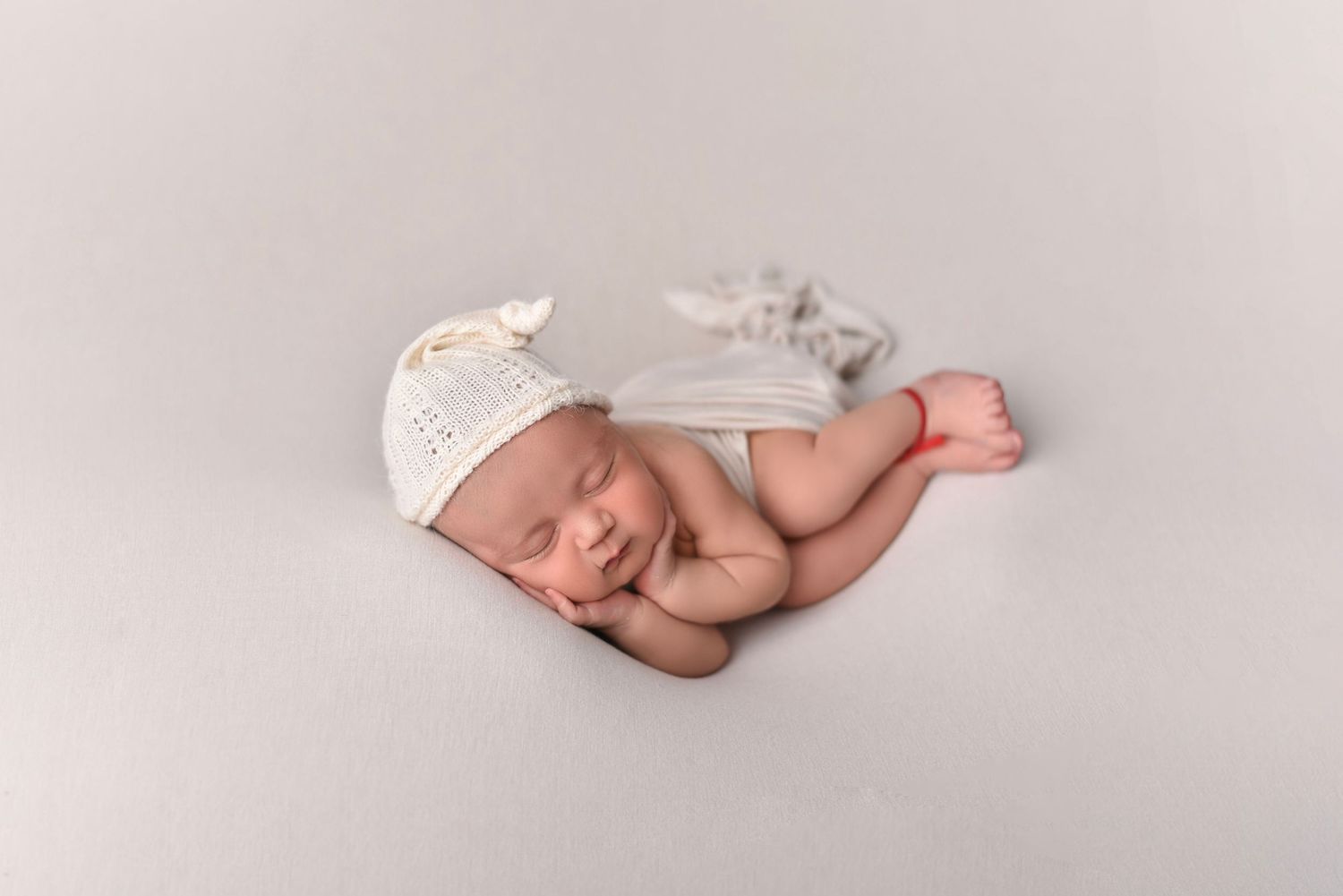 Peaceful sleeping newborn wearing white lace bonnet on neutral gray backdrop.