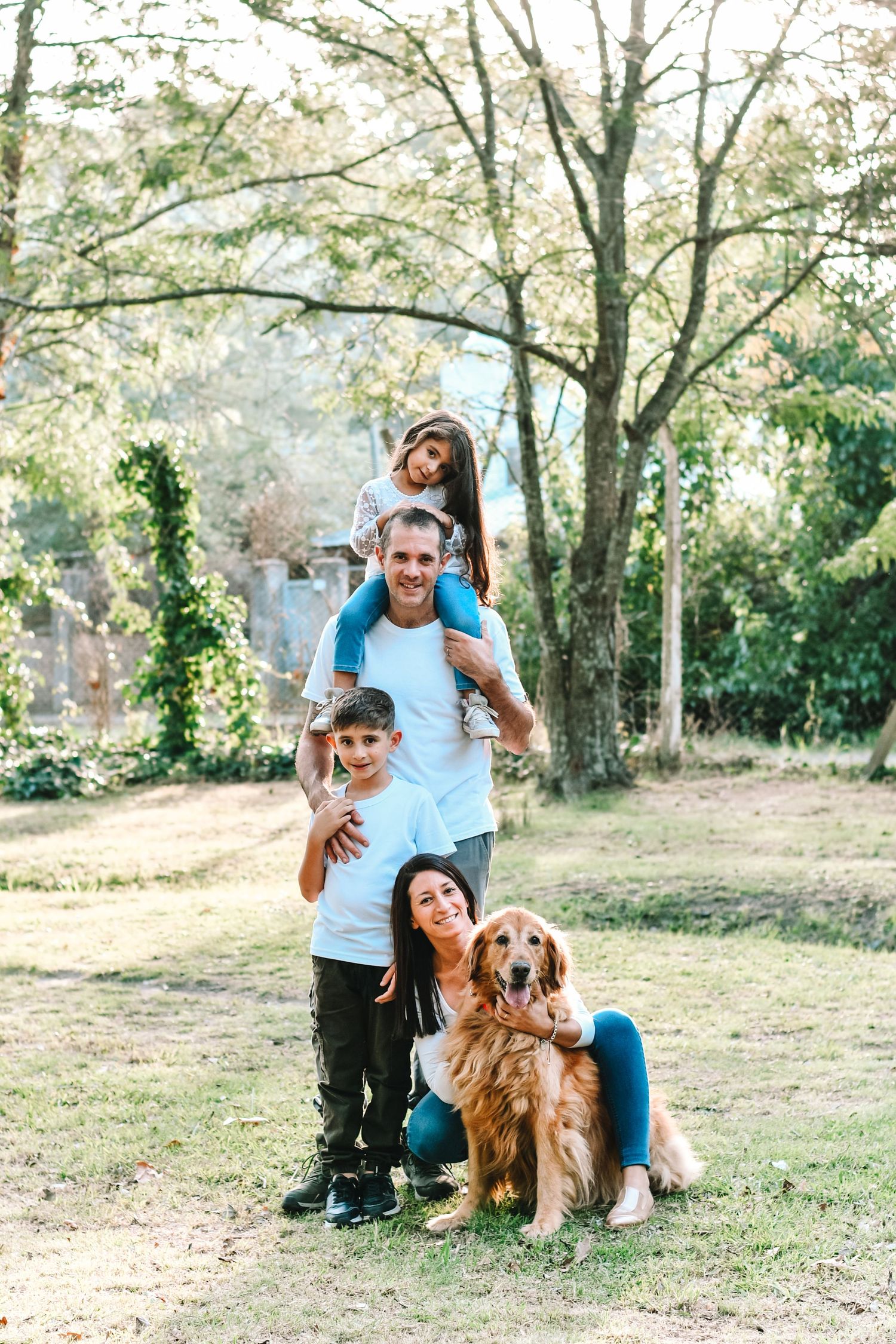Happy family with golden retriever dog enjoying outdoor time together in a sunlit park.