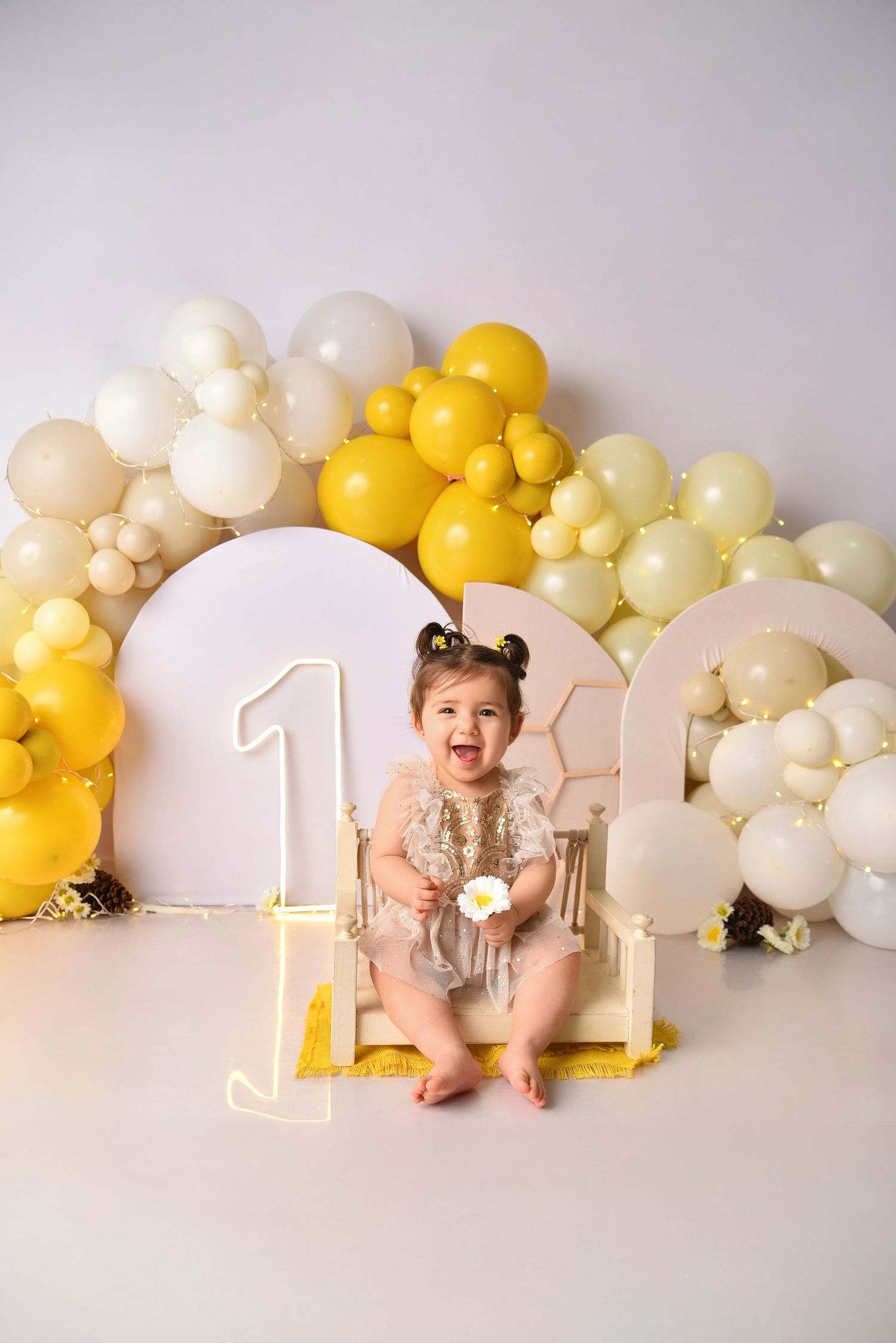 Festive first birthday setup with yellow and white balloon arch and number one decor.