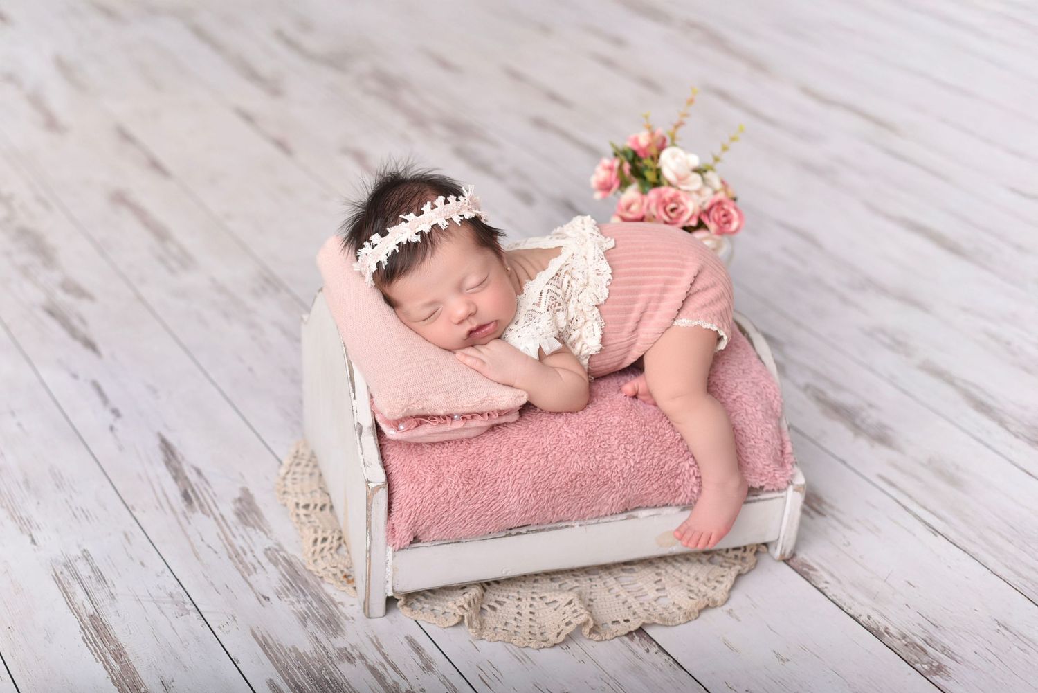 Sleeping newborn posed on vintage pink bed prop with floral crown and delicate wrap.