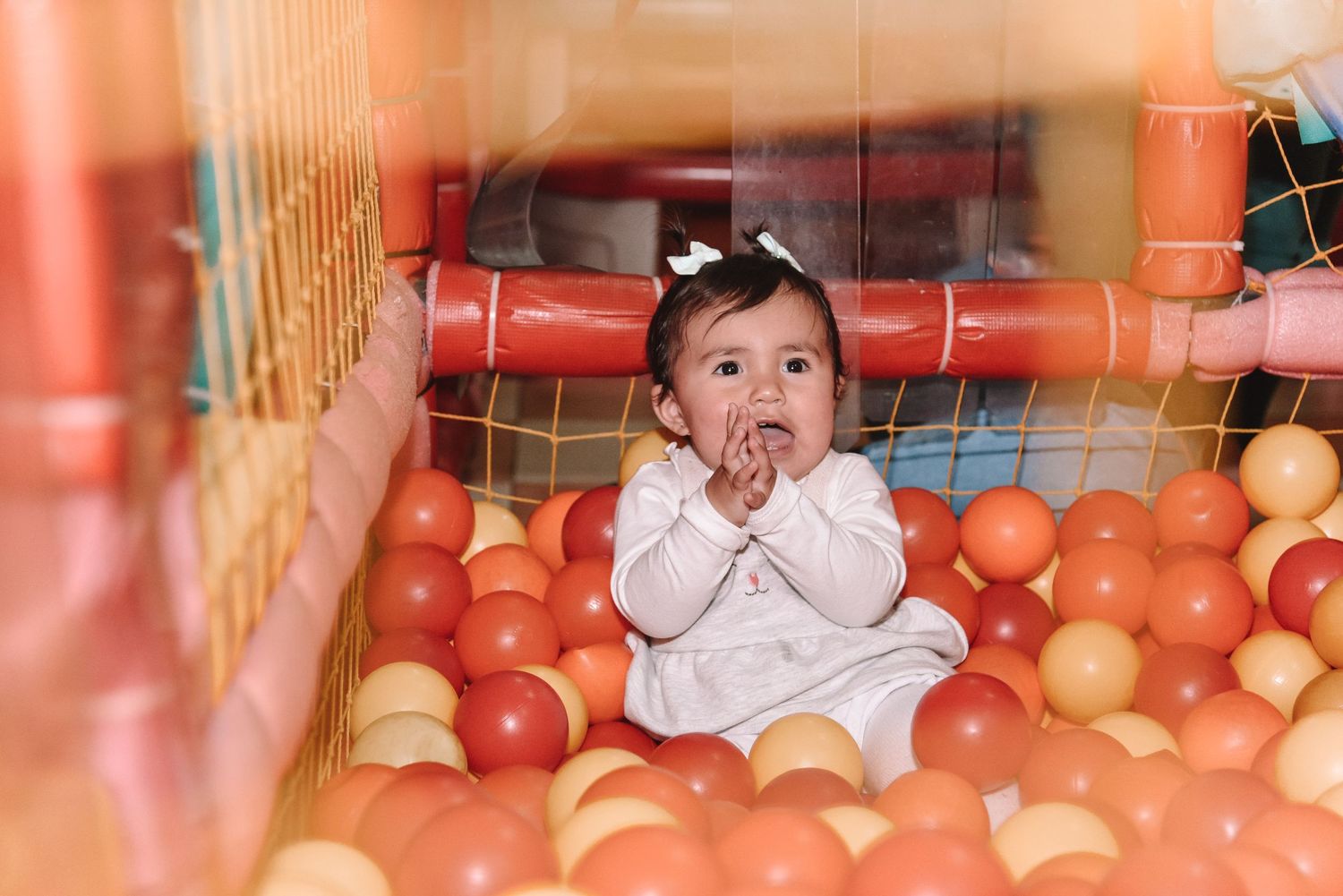 Baby playing in orange ball pit with delighted expression.