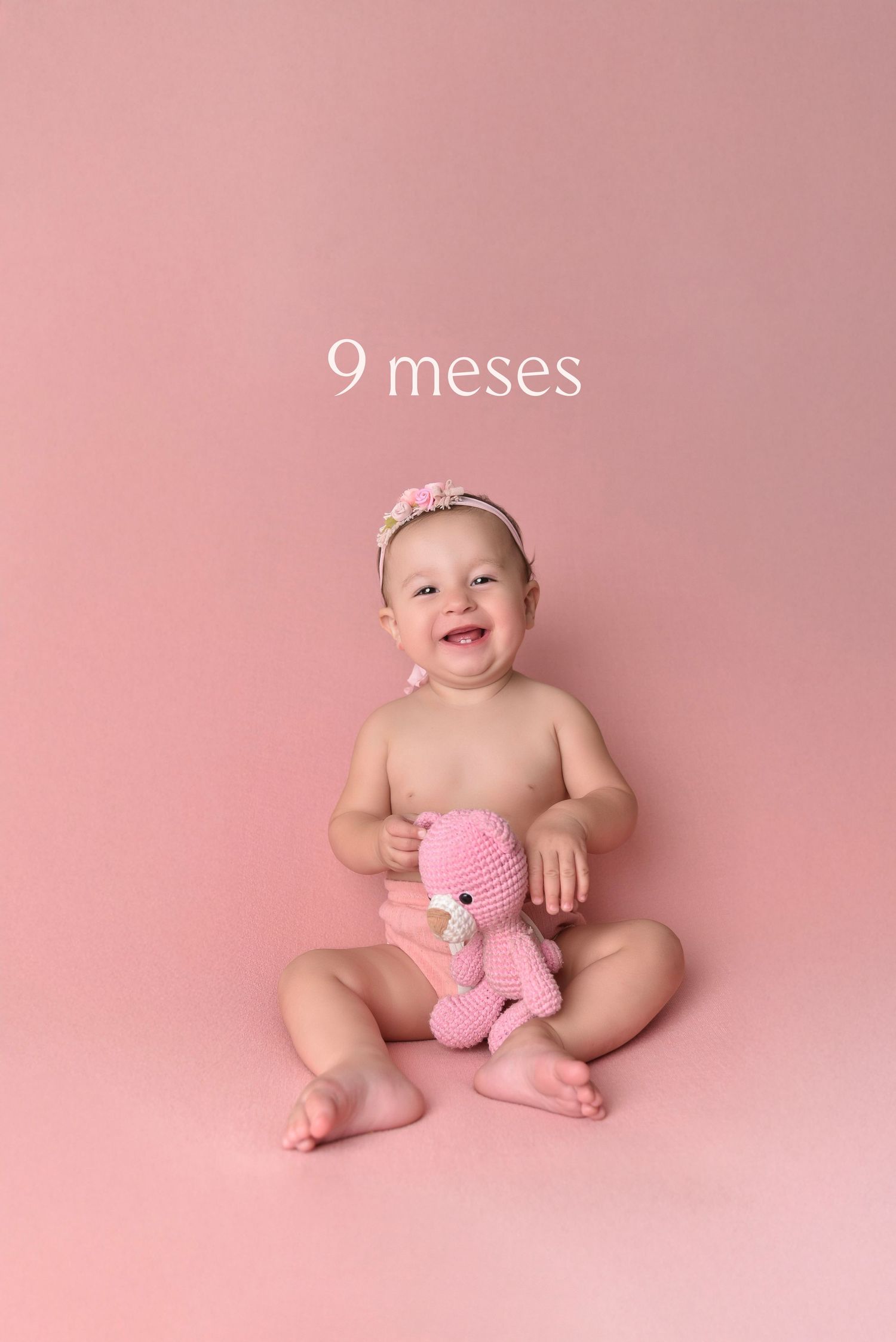 Nine month old baby poses on pink backdrop with plush pink teddy bear in artistic studio photography session.