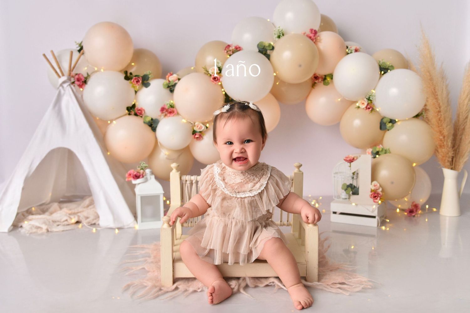 Baby wearing pink tutu sits on floor surrounded by peach and white balloons during first birthday photo shoot.
