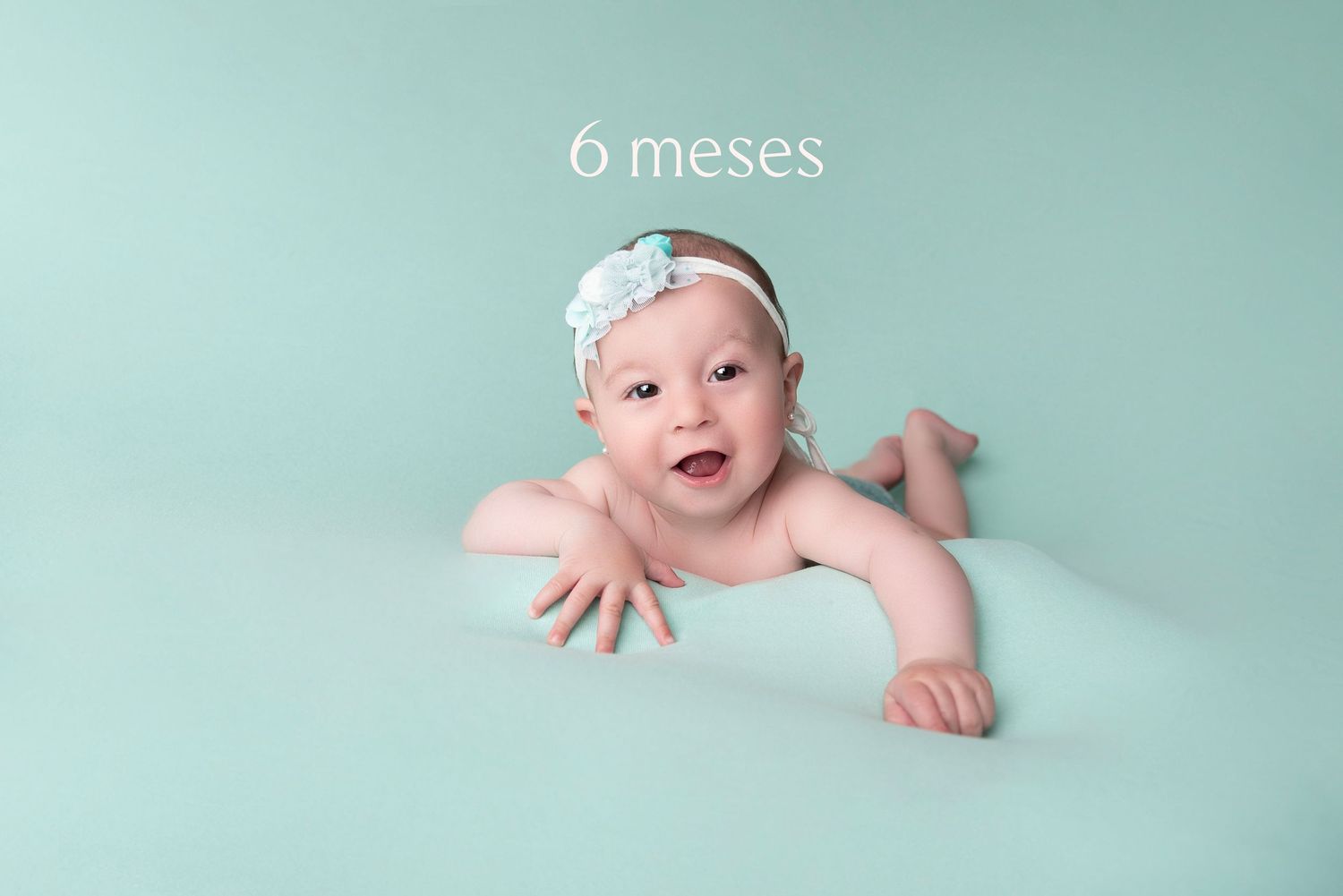 Baby in mint green setting reaches out while laying on stomach during 6 month milestone photo session.