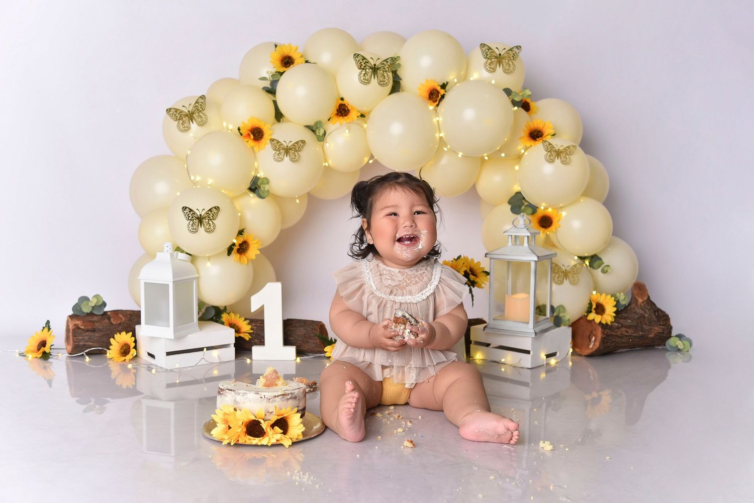 First birthday setup with cream balloon arch, butterfly decorations, and cake smash scene.