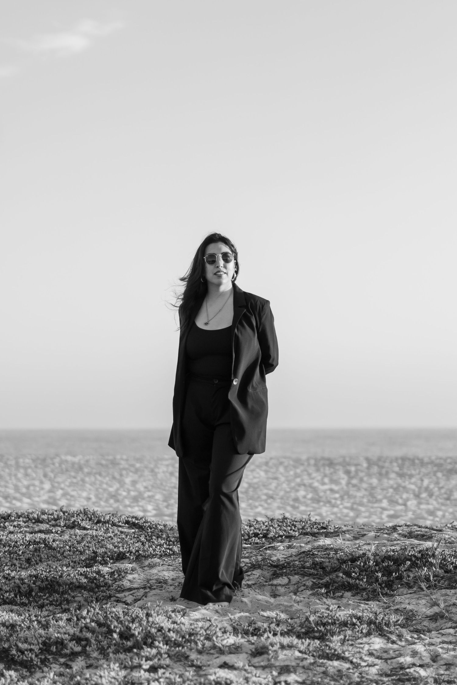 Four black and white photos of a figure in dark clothing walking and standing on a textured rocky terrain near a misty horizon.