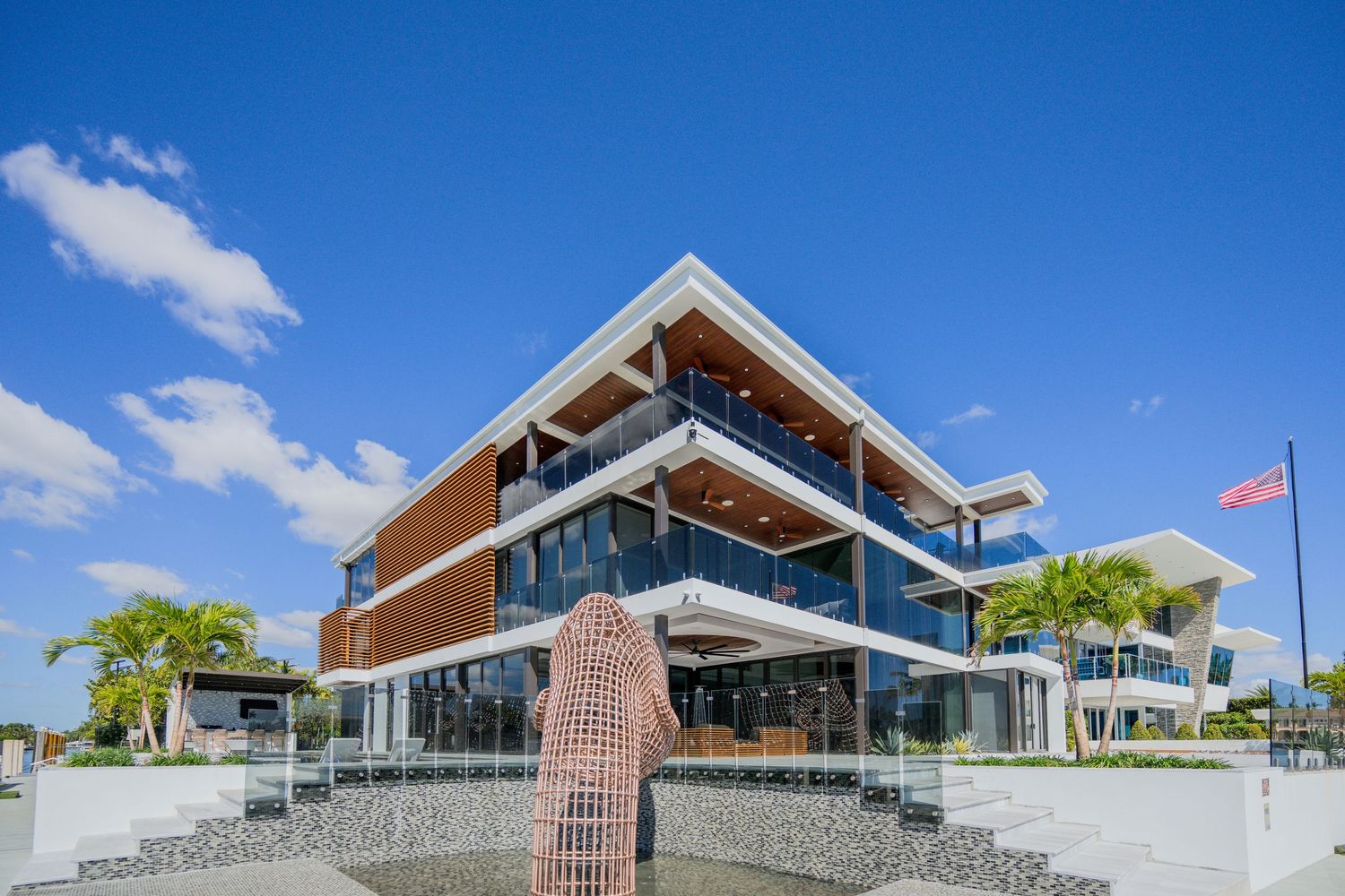 Modern three-story commercial building with glass walls and wood accents under bright blue sky with palm trees.