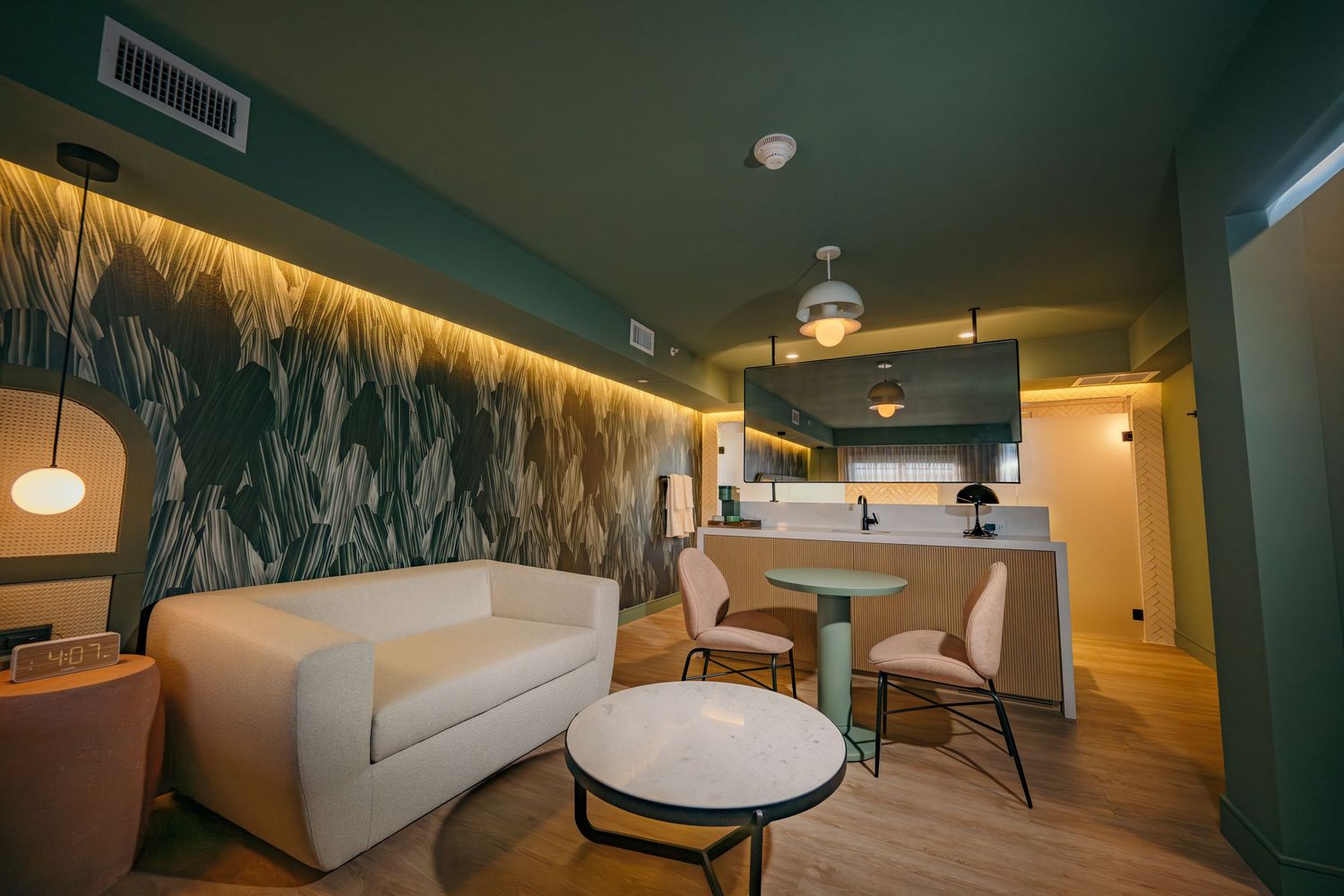 Modern hotel suite with teal ceiling, botanical wallpaper, white sofa, marble coffee table, and bar seating area.