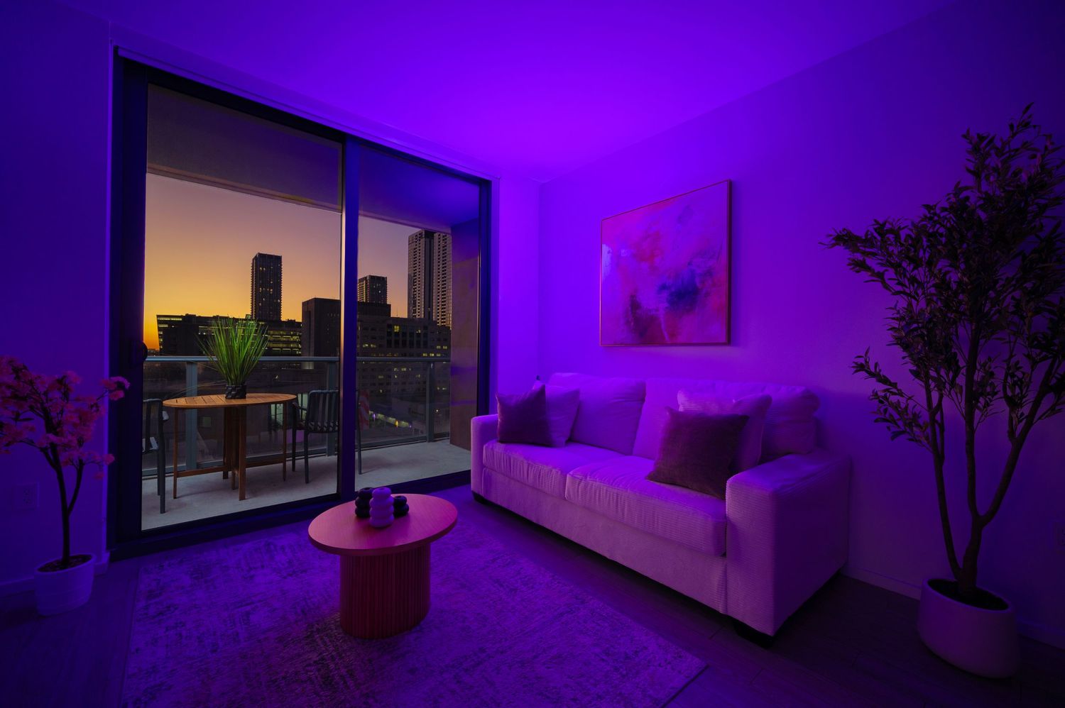 Modern living room bathed in purple LED lighting with city skyline view at sunset through floor-to-ceiling windows.