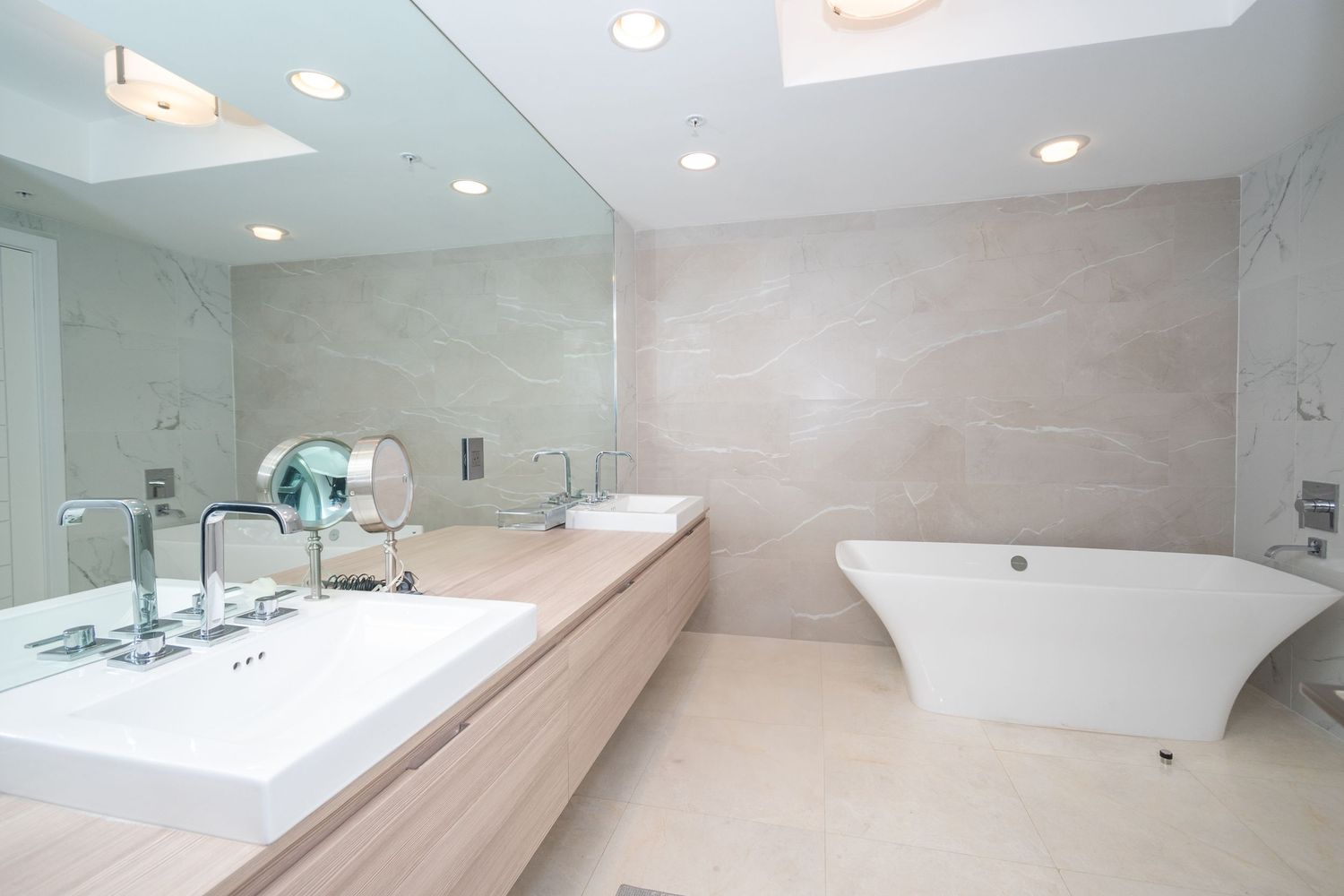 Modern minimalist bathroom with freestanding tub and long vanity featuring recessed lighting.
