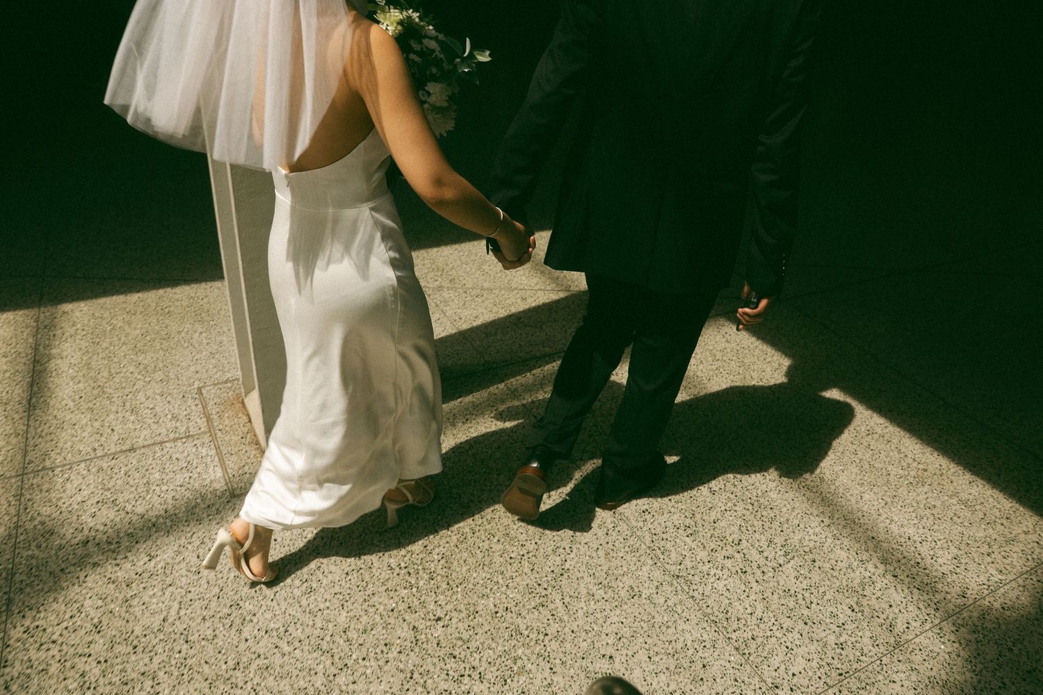 Close-up view of formal shoes and dress hemlines on a textured floor during a wedding celebration.