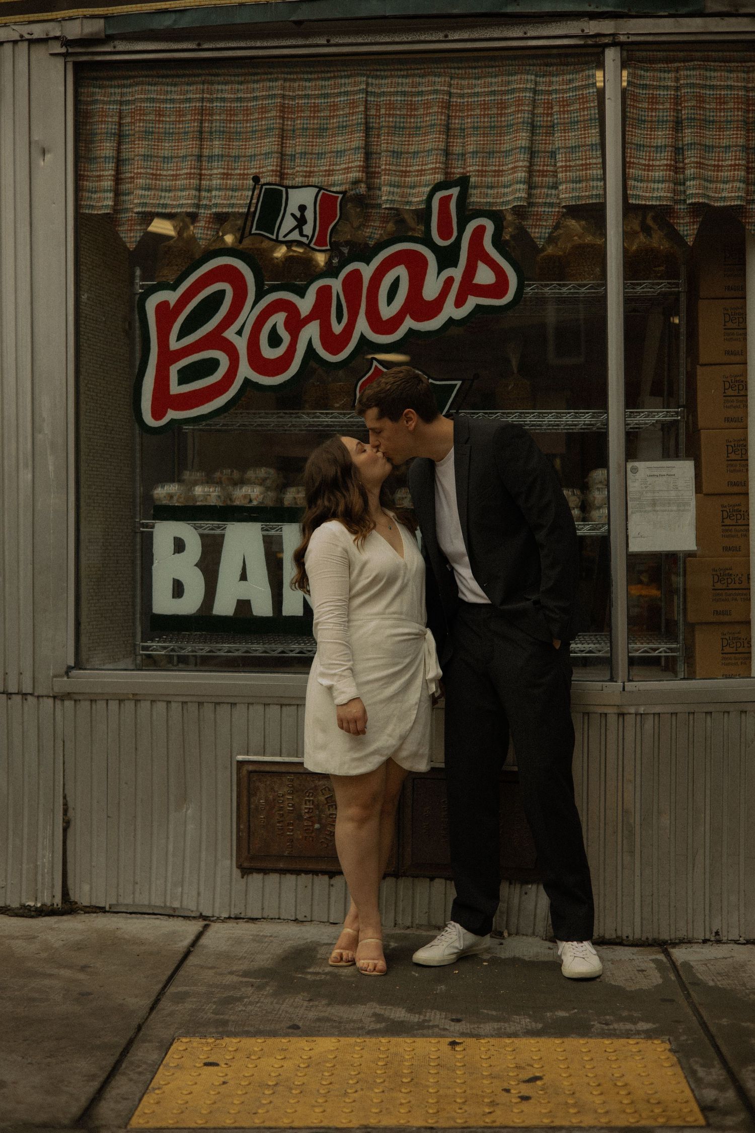 A couple shares a romantic moment outside Bova's storefront with vintage signage in the background.