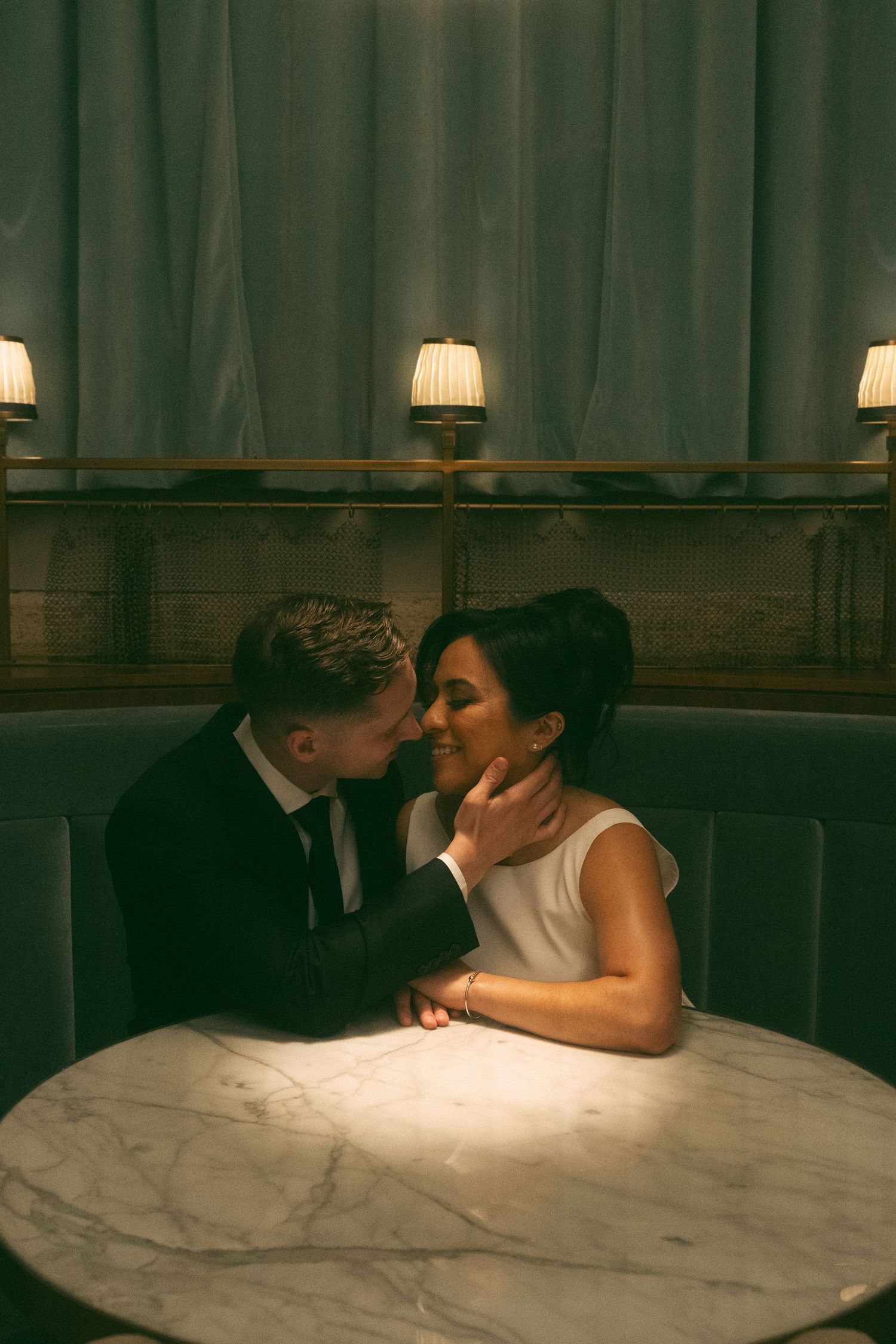 A romantic couple shares an intimate moment while seated at a marble bar counter under soft lighting.