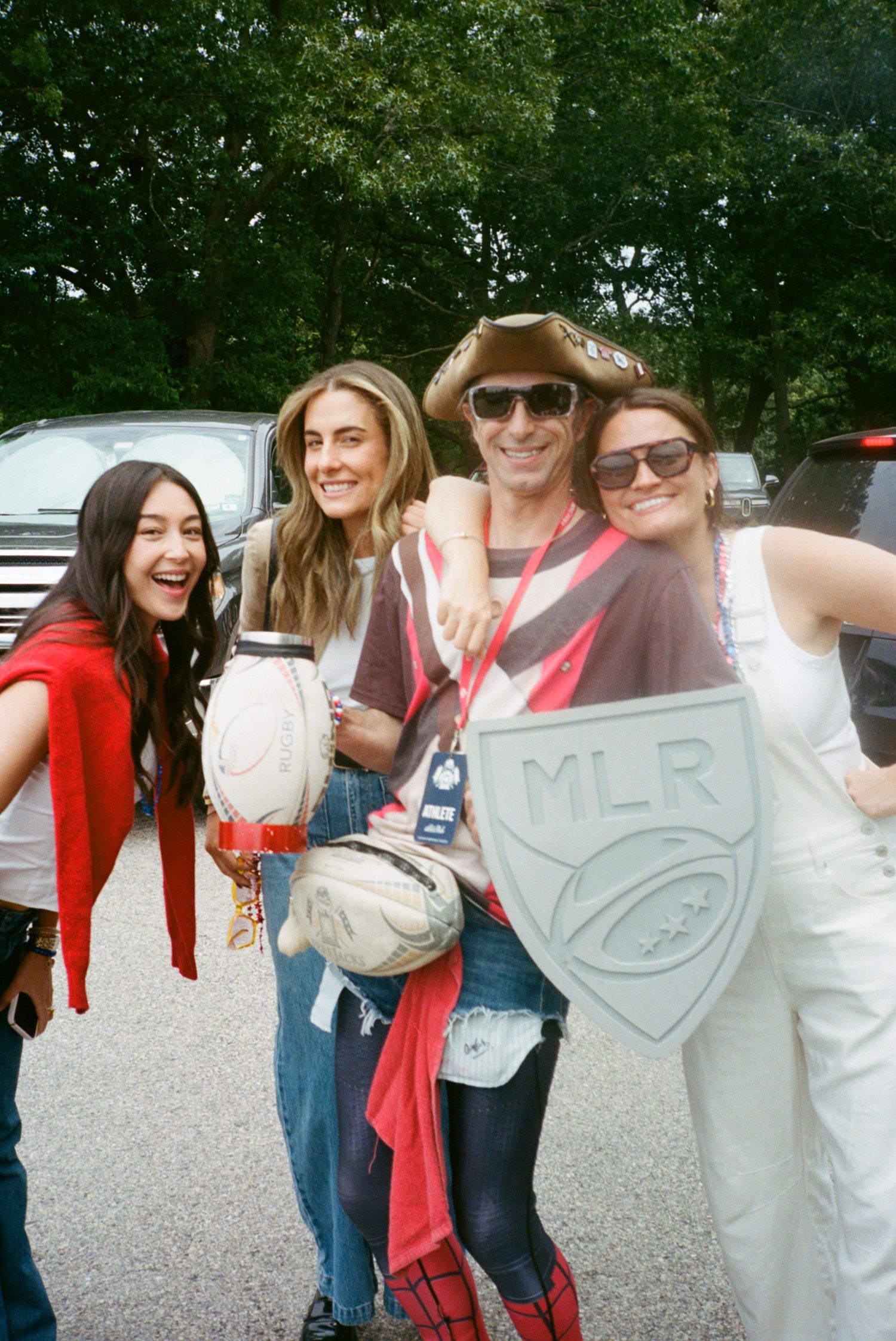 Four fans pose with MLR rugby logo and ball at an outdoor Major League Rugby event on a sunny day.