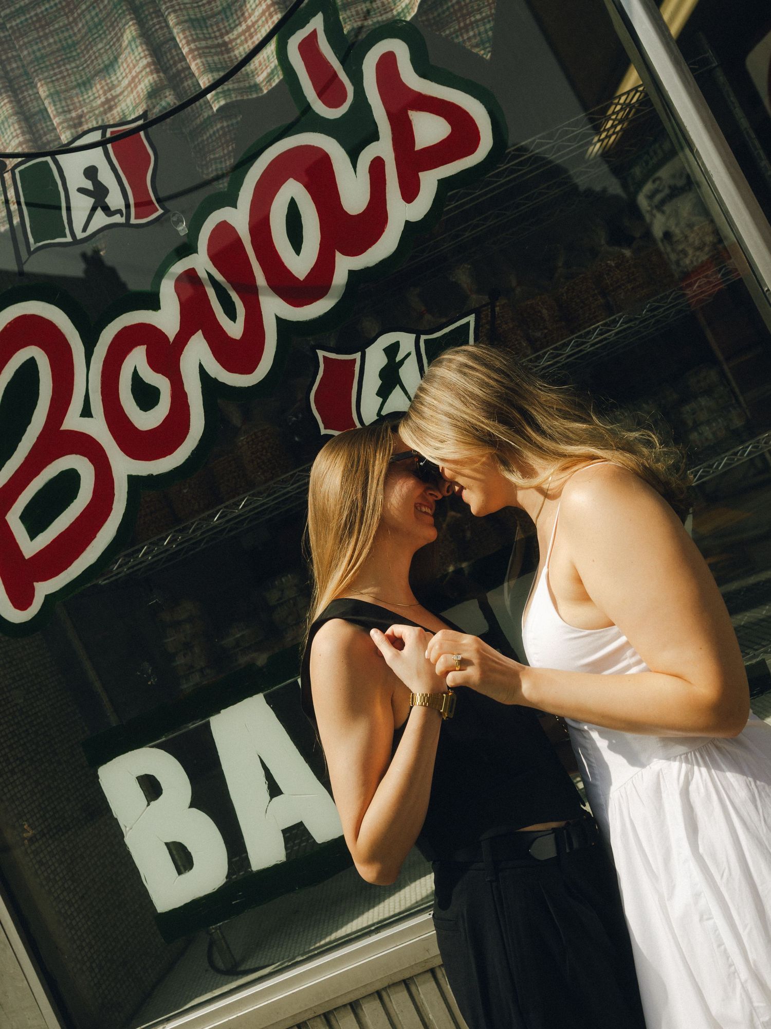 A person in a white tank top leaning against a wall with Budweiser signage visible in the background.