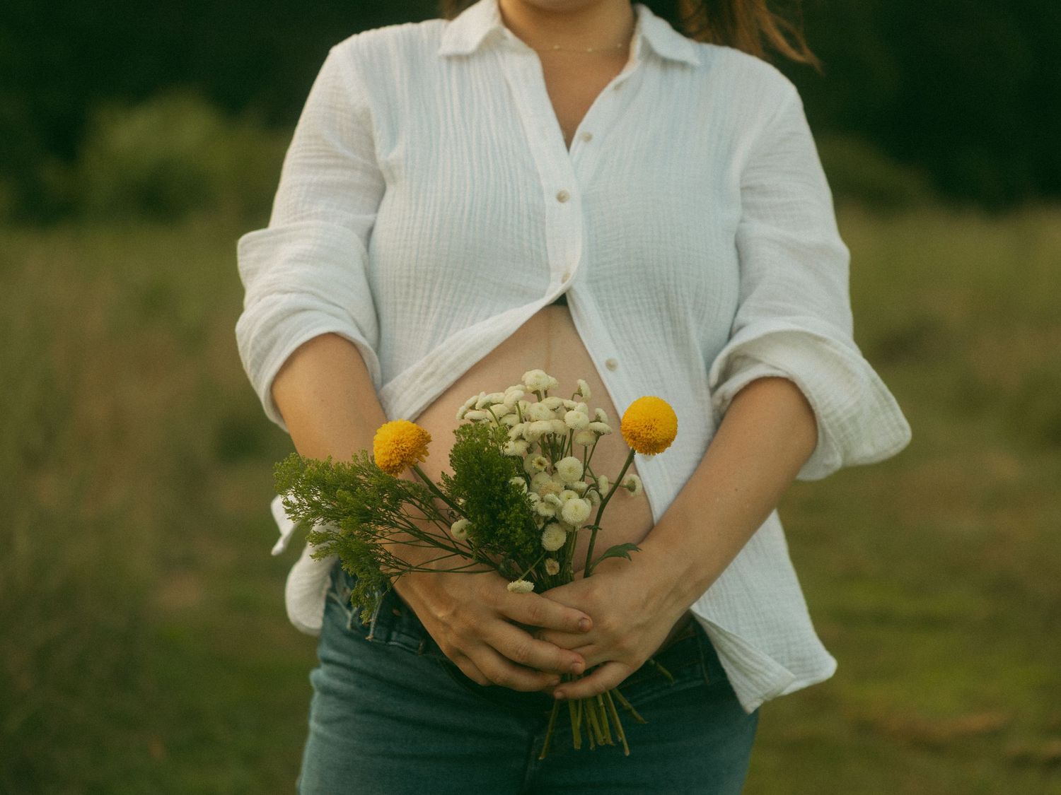 A person in a white shirt holds a bouquet of freshly picked wildflowers in a sunlit meadow.